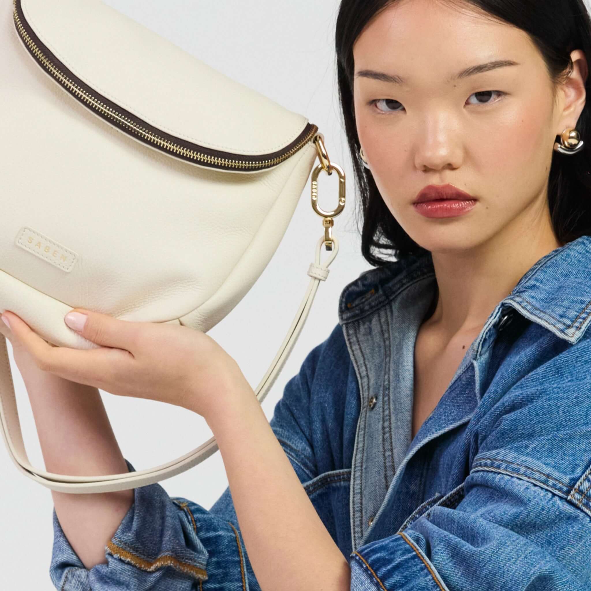 Saben Fifi Crossbody Bag - Quartz held by a model, showcasing its stylish pebbled leather and chic design.