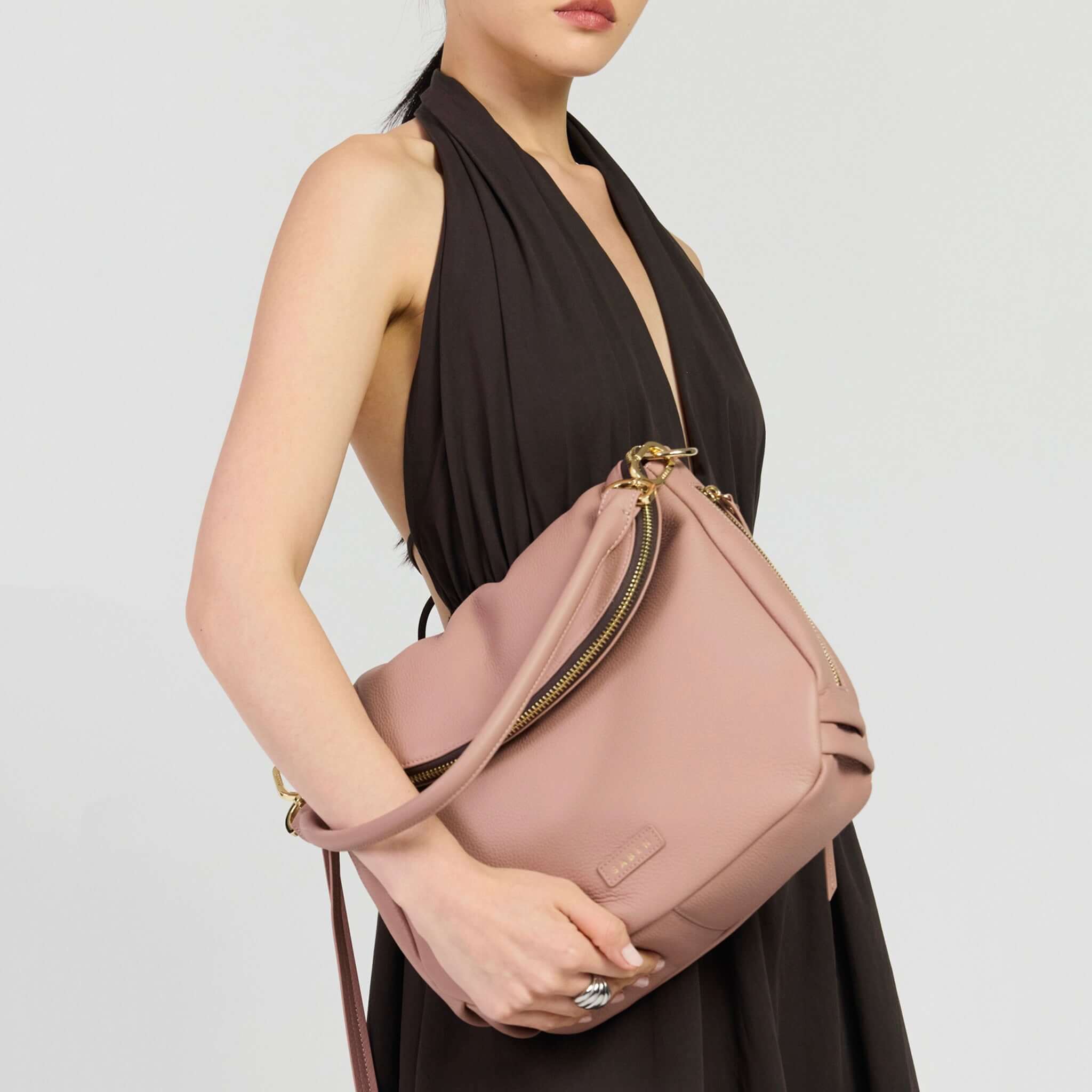 Saben Frankie Shoulder Bag - Rosewater being held by a model wearing a black dress, showcasing its stylish design.