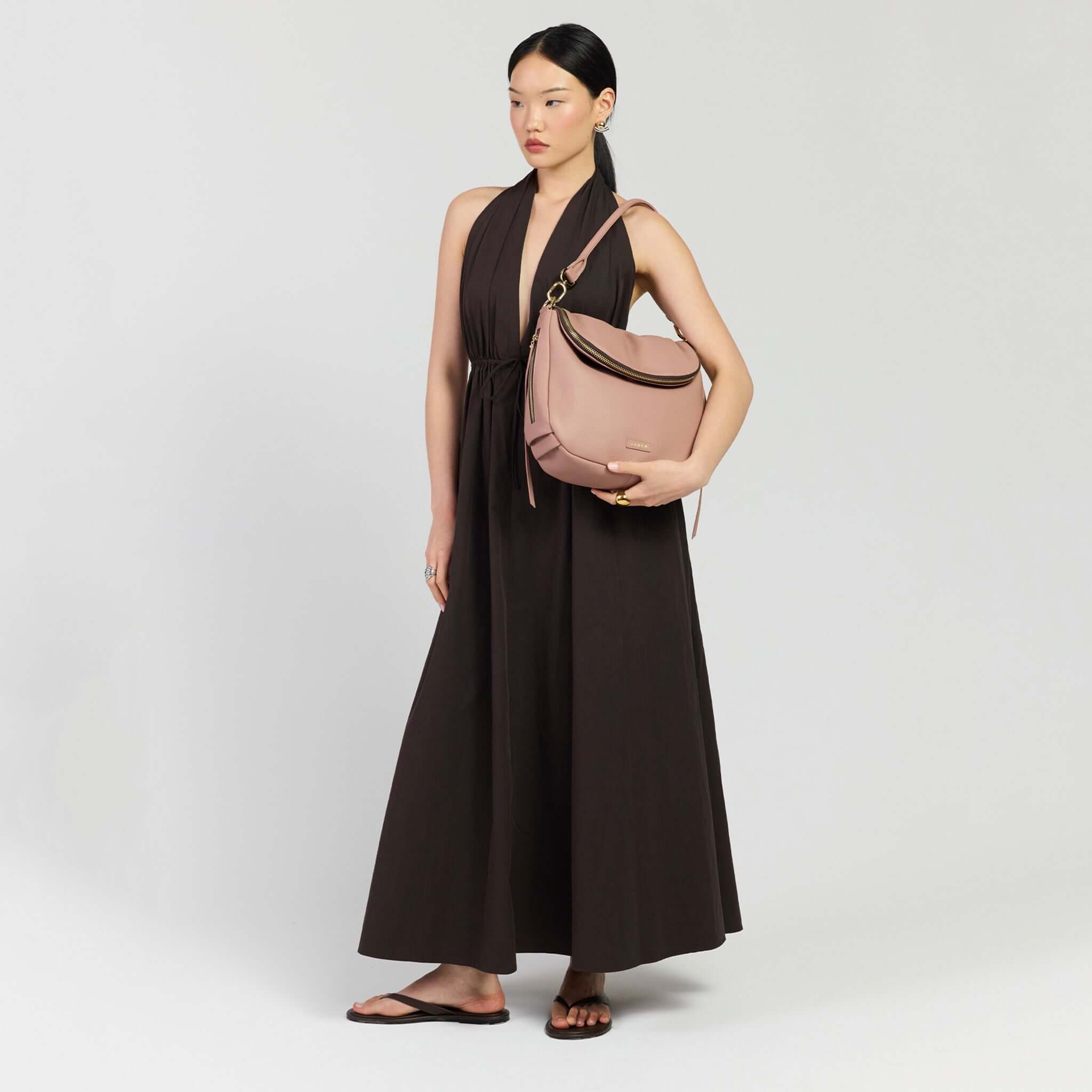 Model wearing a brown dress holding the Saben Frankie Shoulder Bag - Rosewater, showcasing its stylish design and functionality.