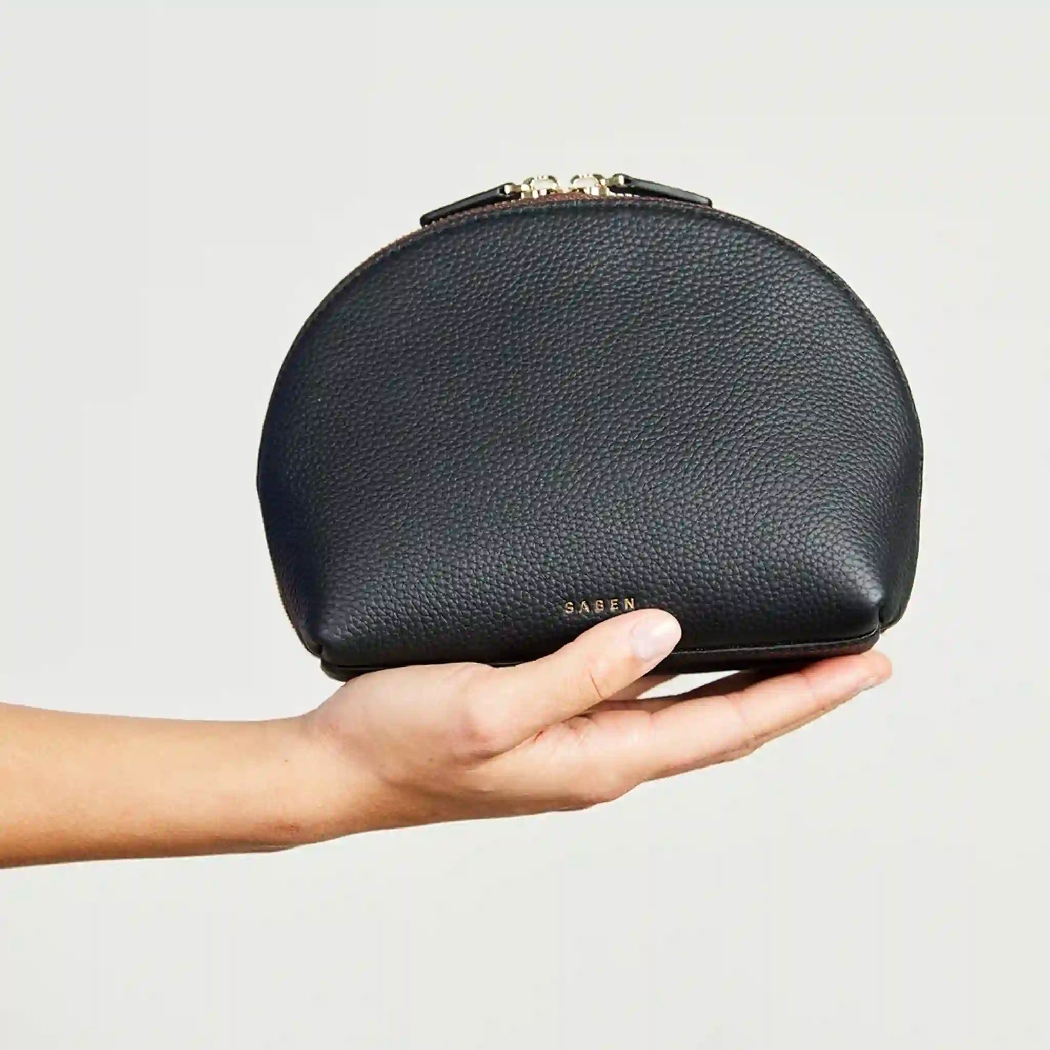 Black leather makeup bag held in a hand against a light gray background