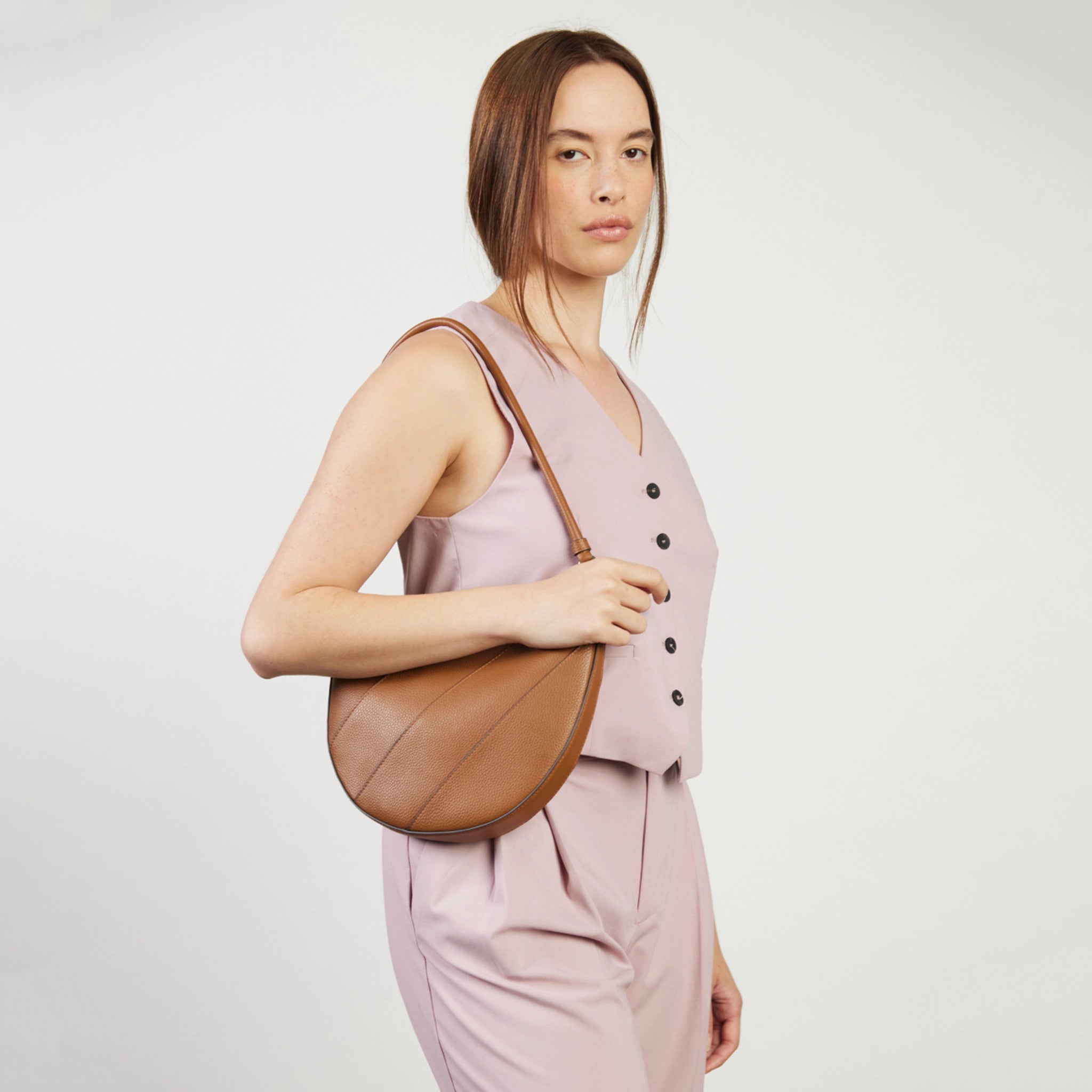Woman holding a brown leather bag against a plain background