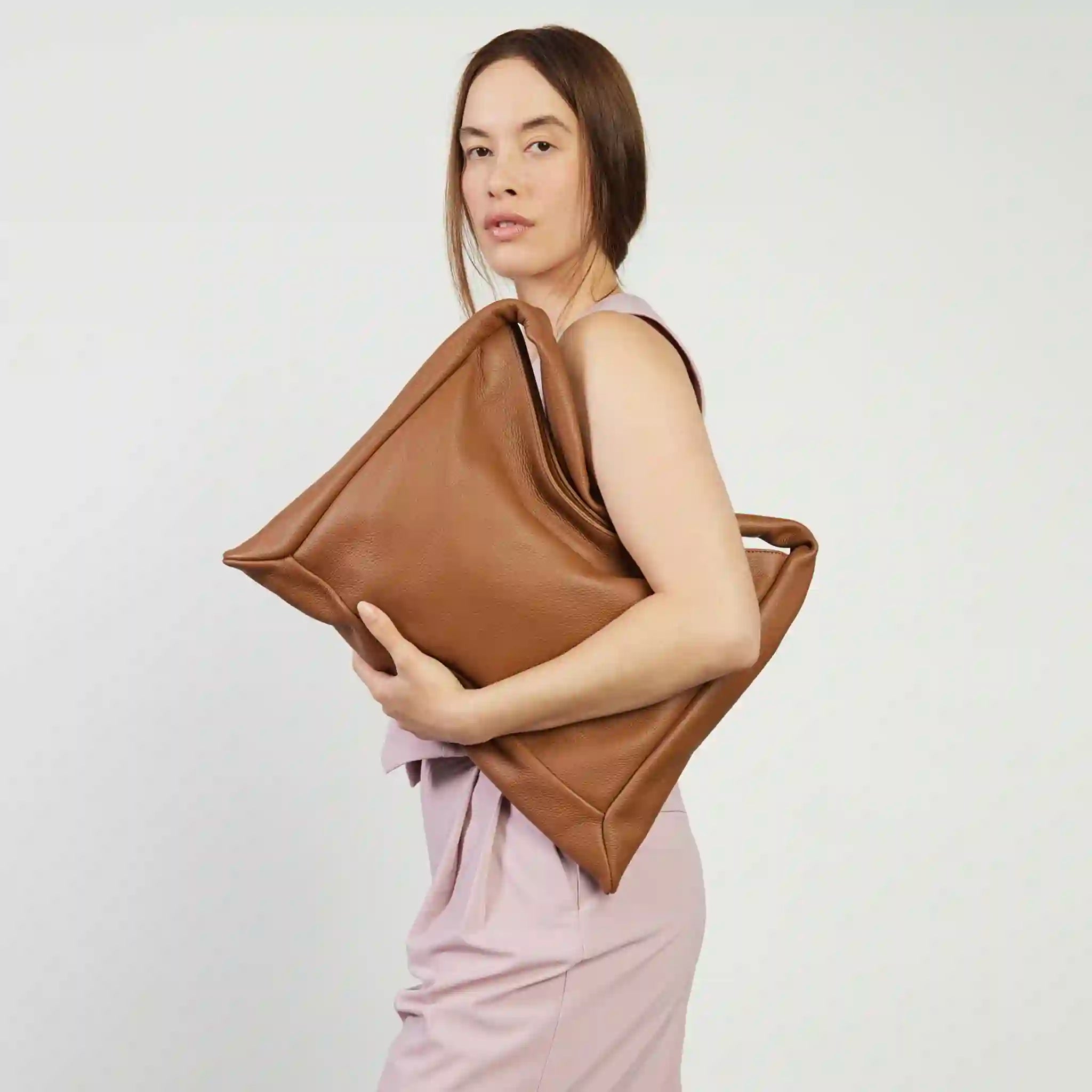 Woman holding a large brown leather bag against a plain background