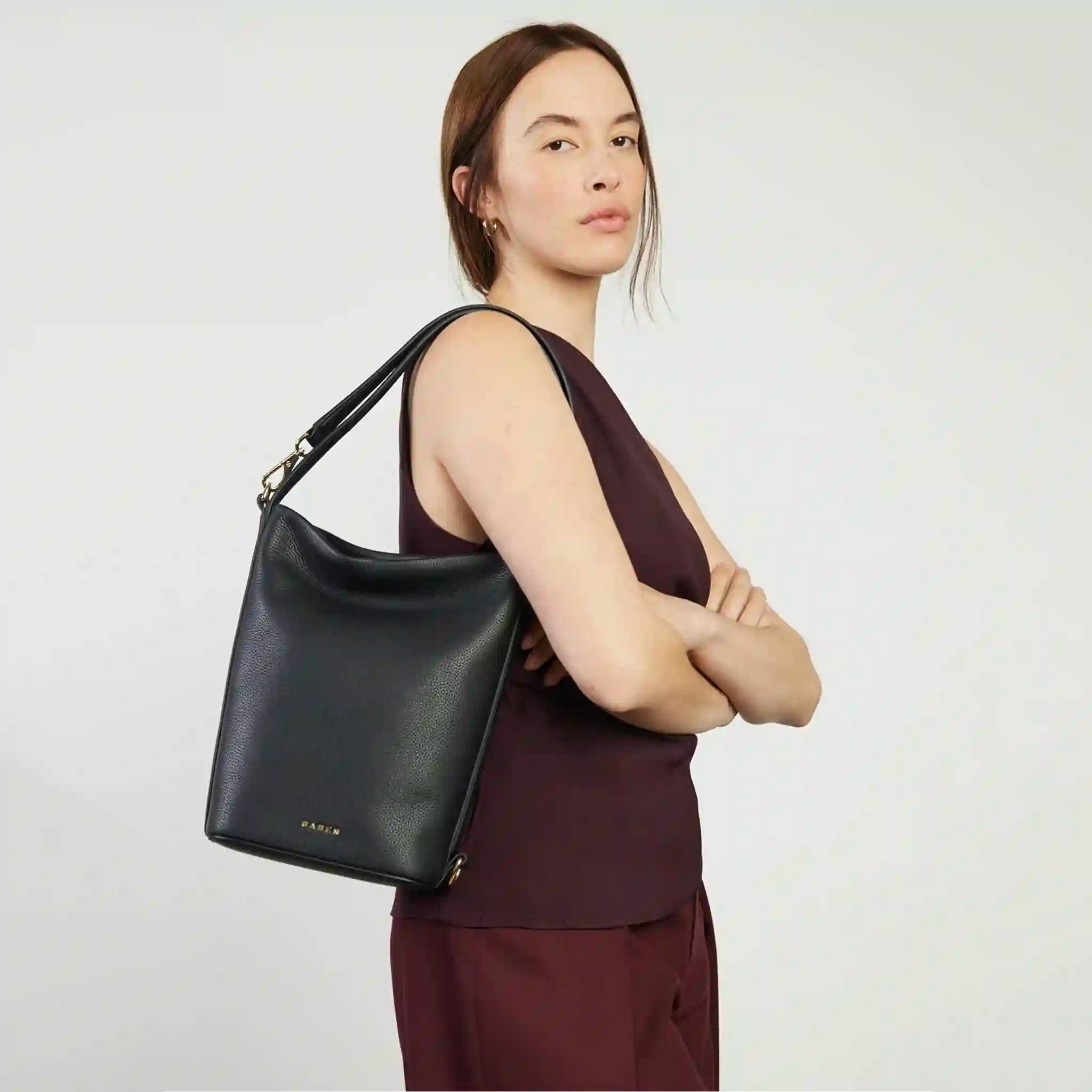 Woman holding a black handbag against a plain background