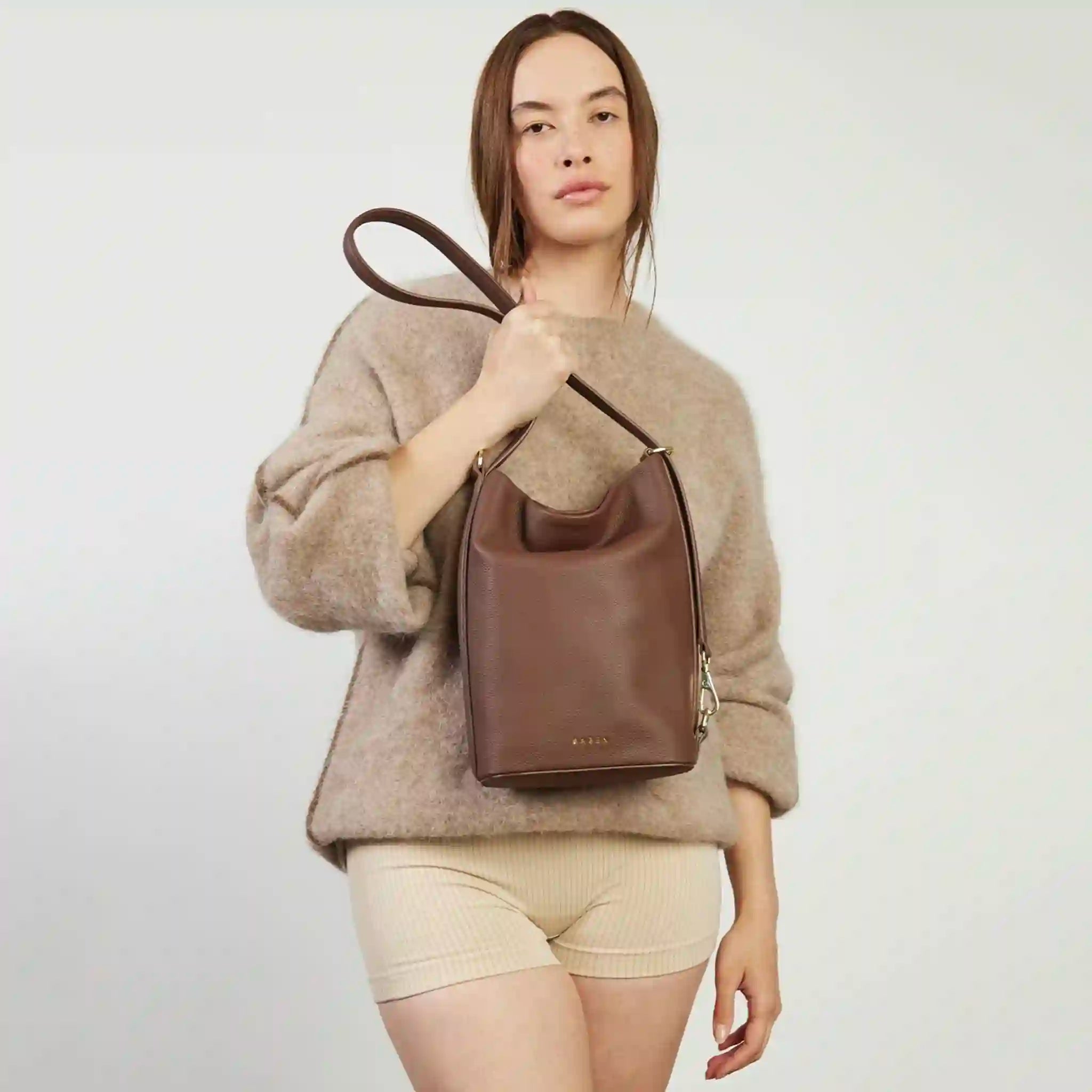 Woman holding a brown leather handbag against a plain background