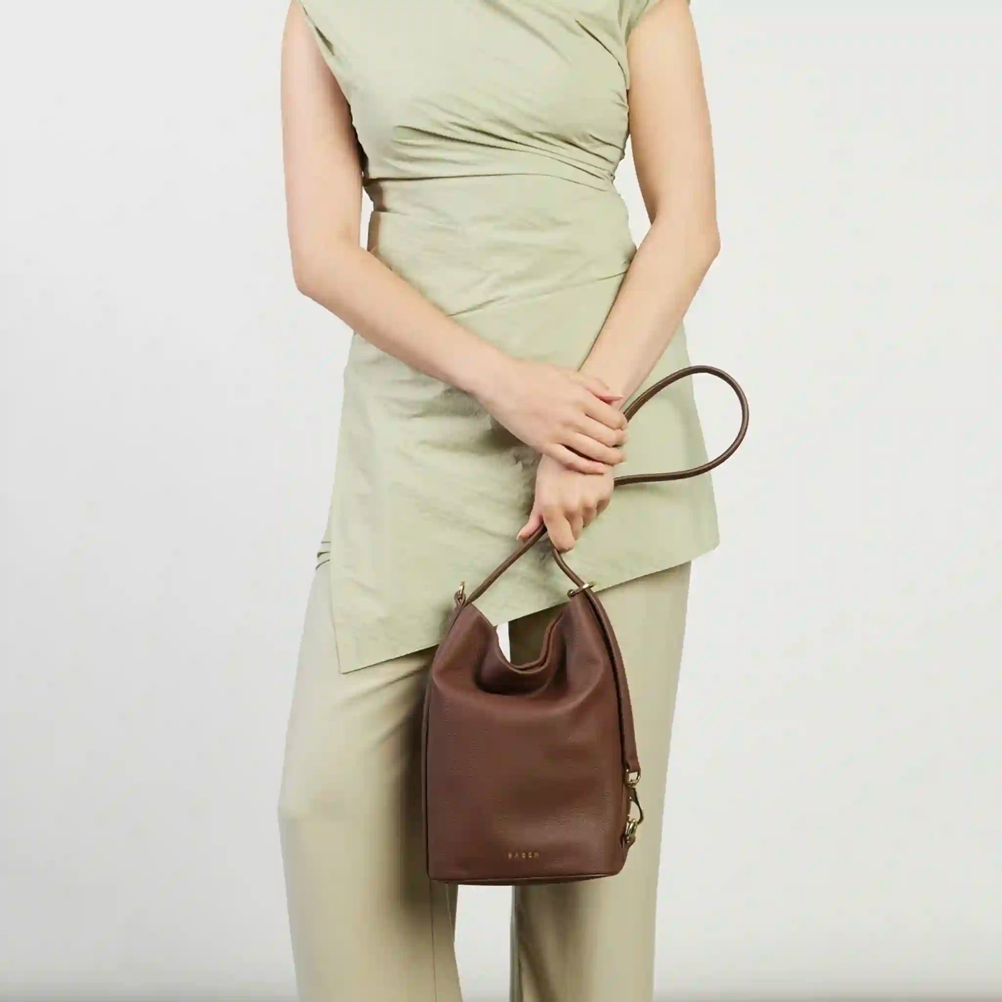 Person holding a brown handbag against a plain background