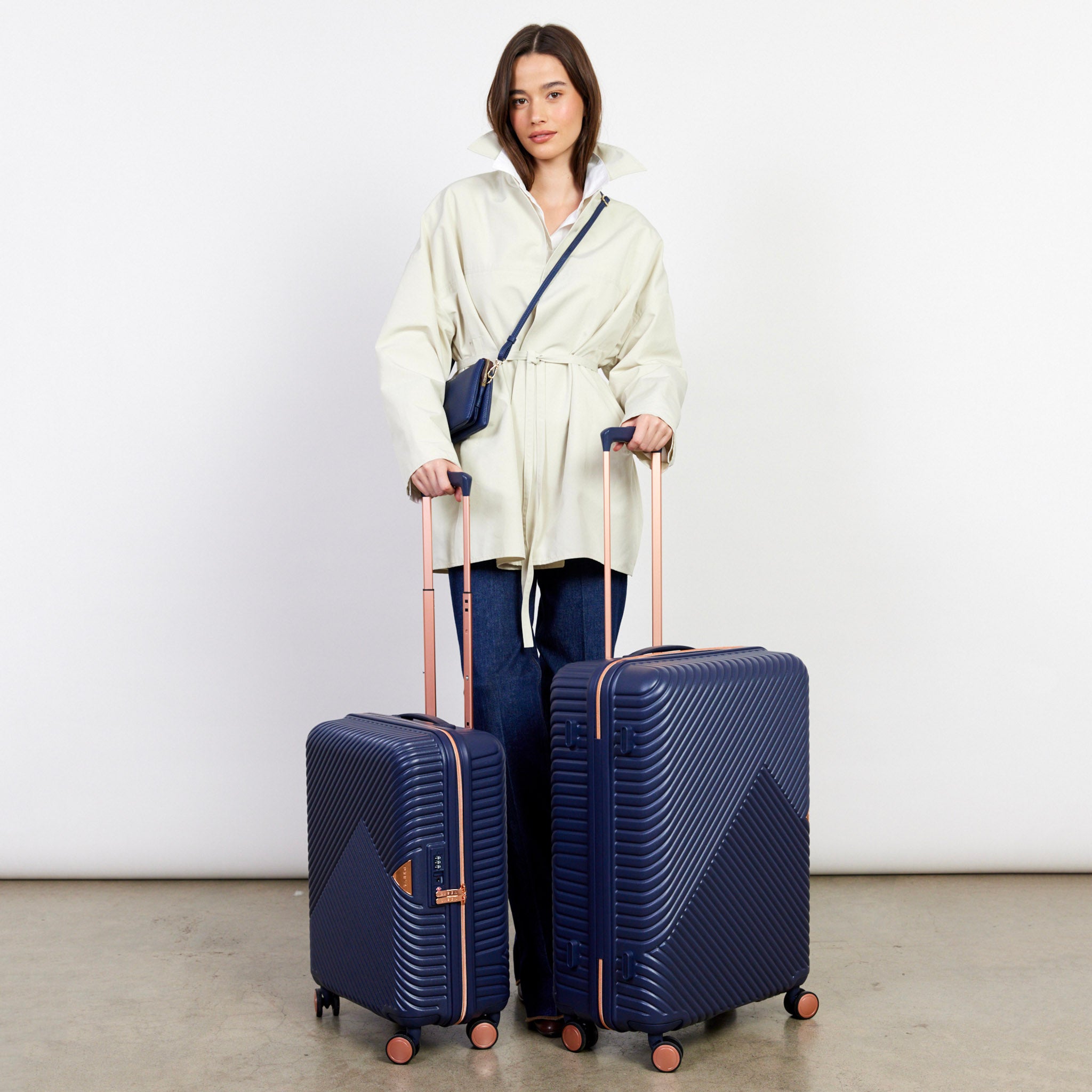 Woman holding two navy blue suitcases with a white background