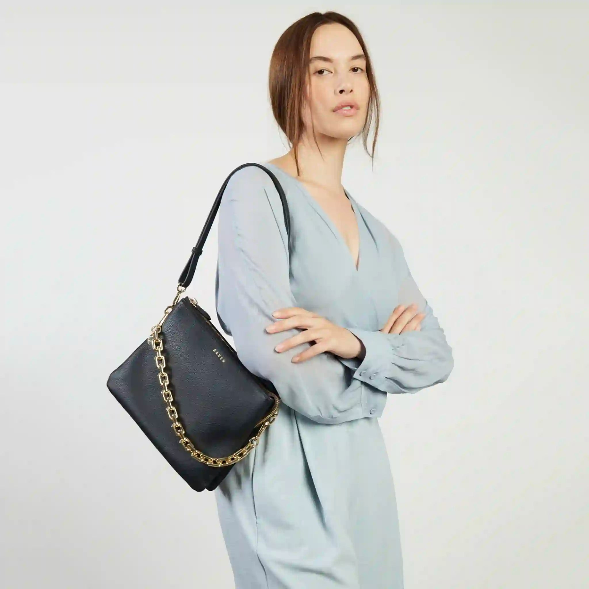 Woman holding a black handbag with a gold chain strap against a white background