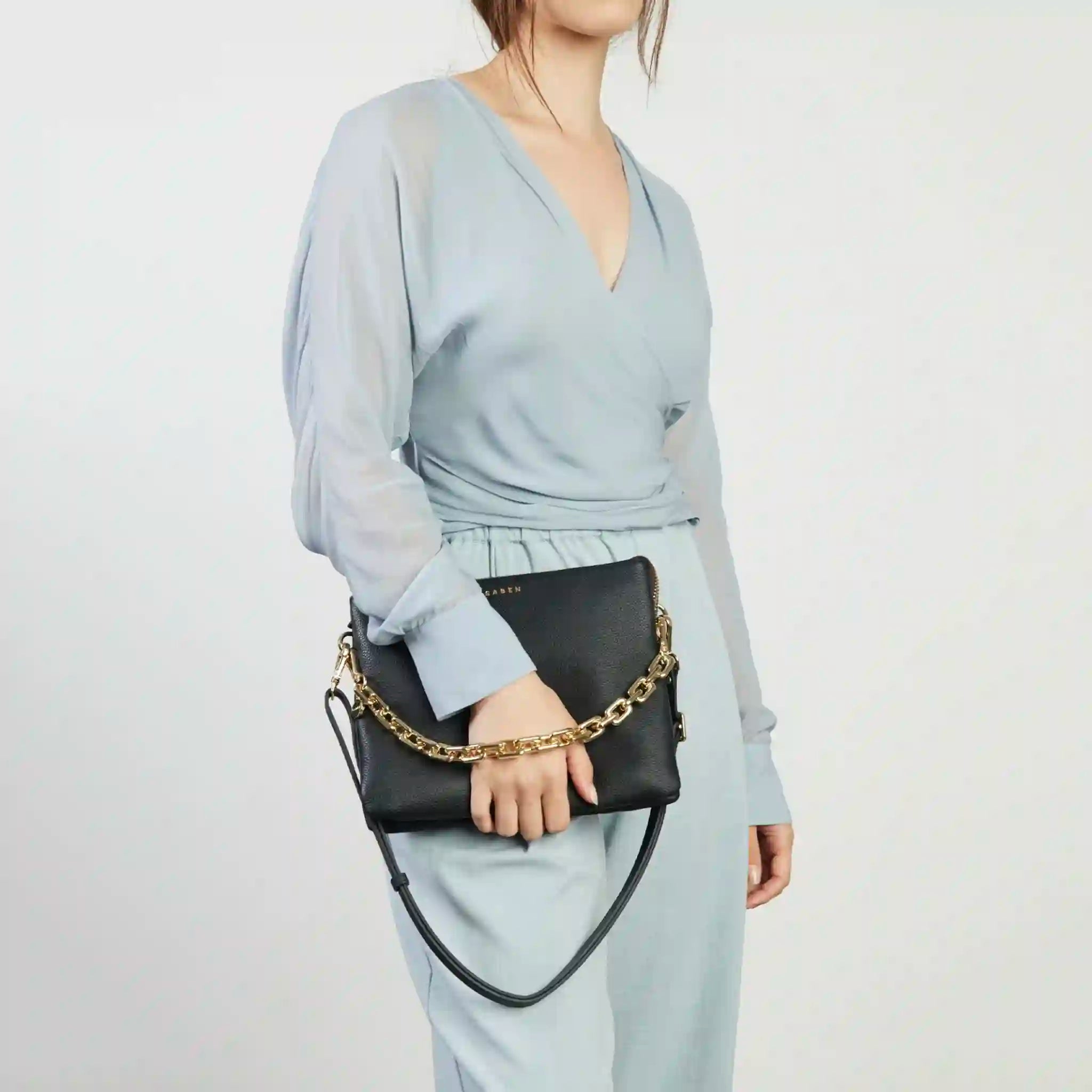 Person holding a black handbag with a gold chain on a plain background
