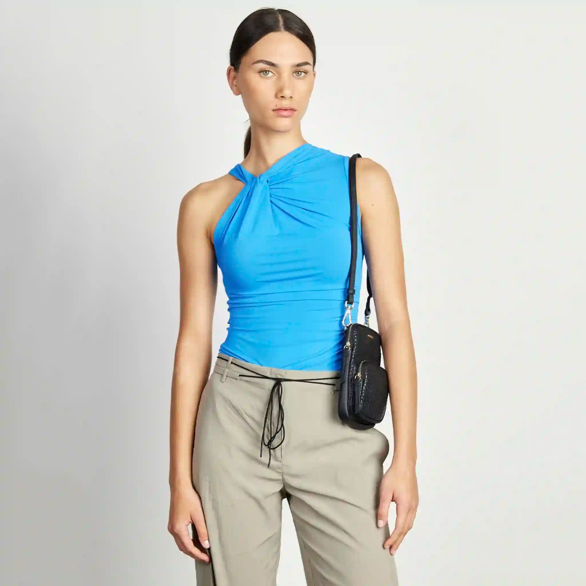Woman wearing a blue top and beige pants with a black bag on a white background
