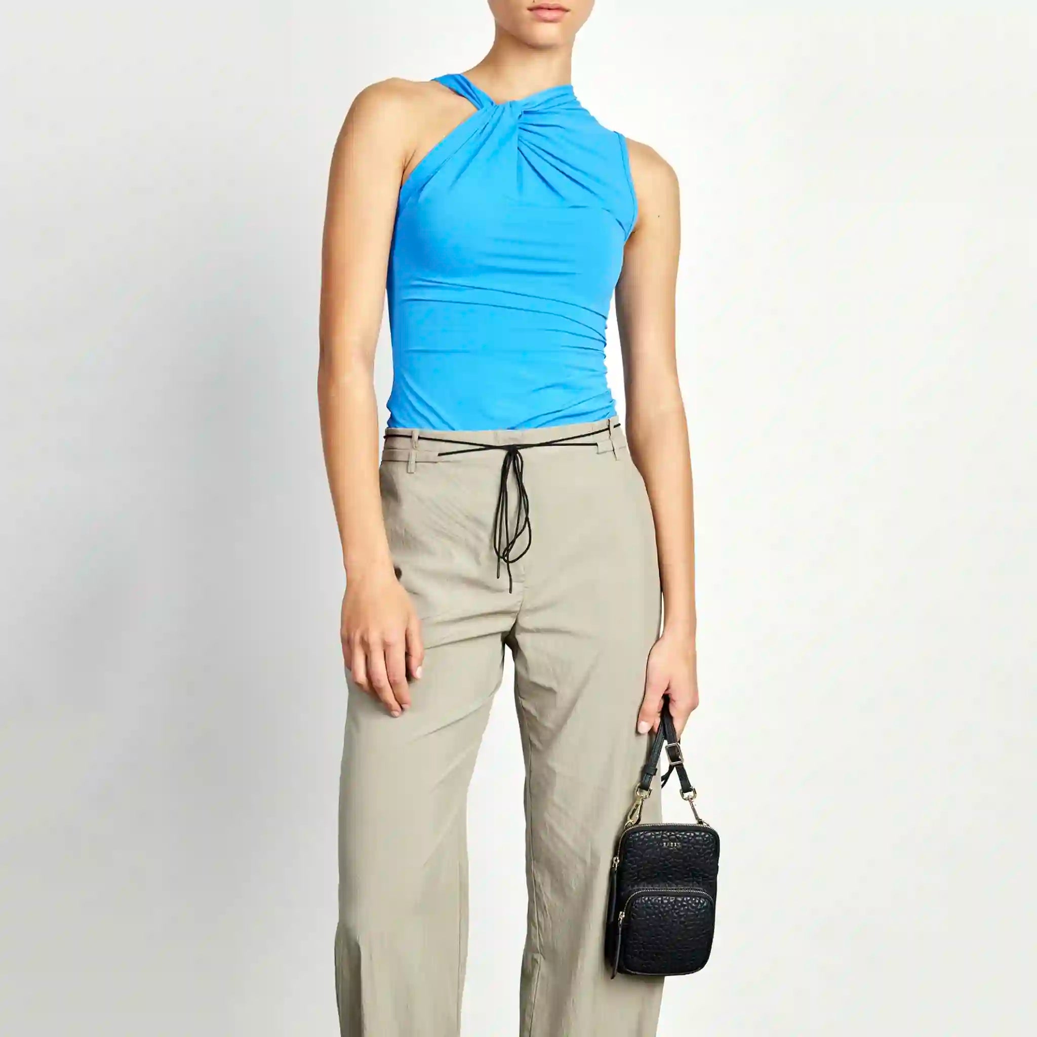 Person wearing a blue top and beige pants holding a black handbag on a white background