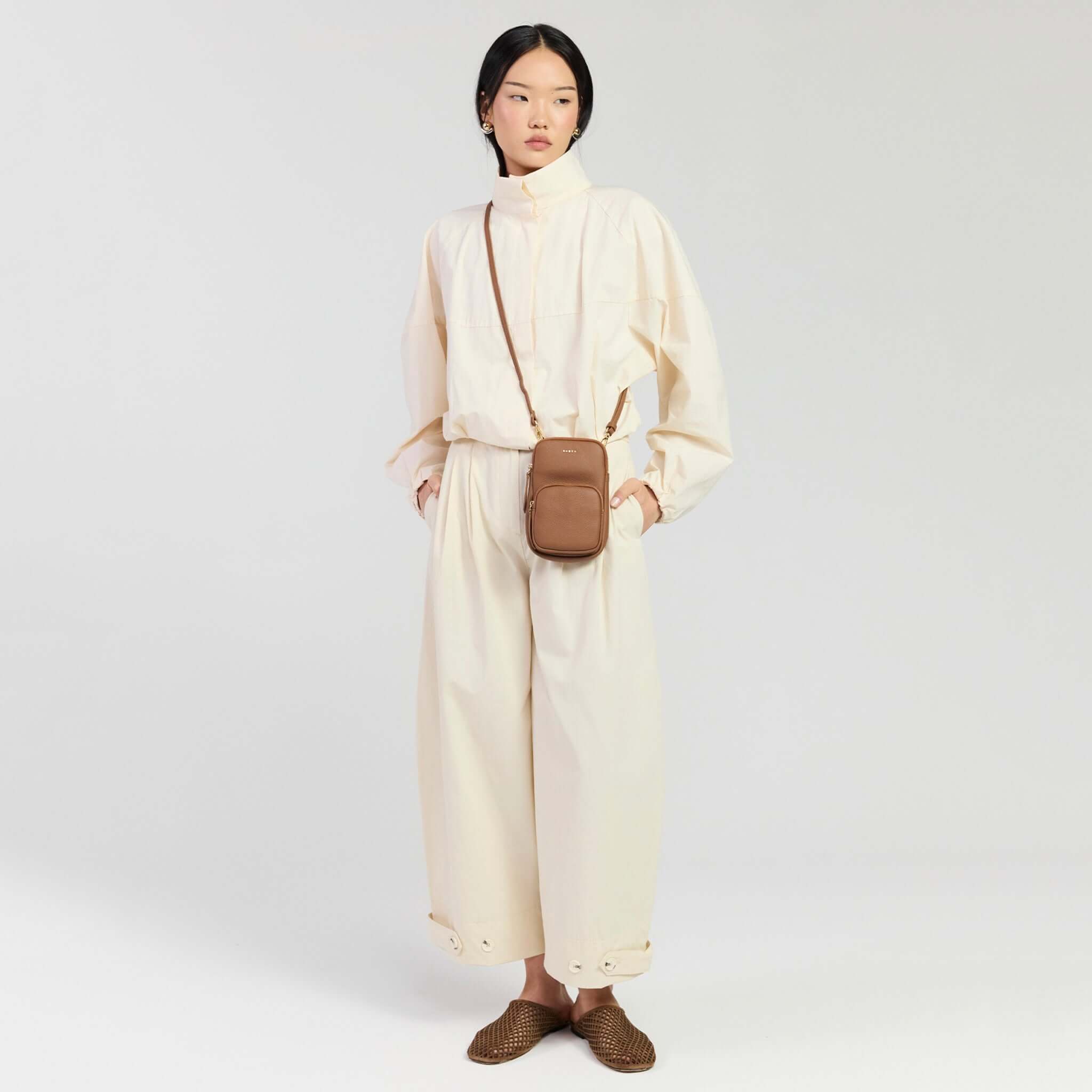 Saben Nikko Pocket Phone Sling - Tan Luxe worn crossbody by a model in a stylish outfit. Perfect for hands-free commuting.