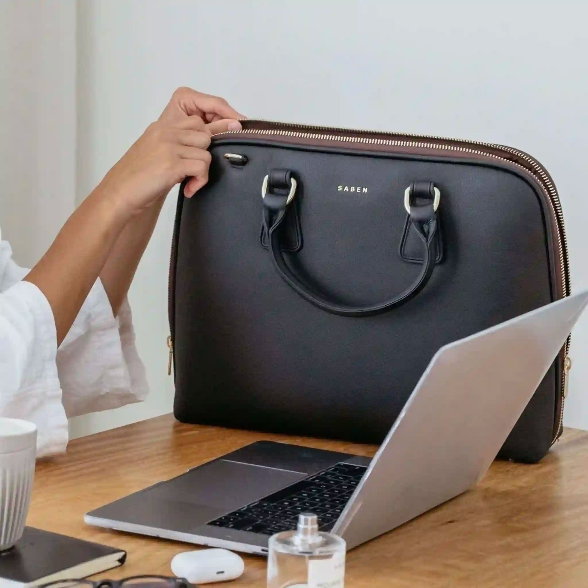Person opening a black briefcase with a laptop on a wooden desk.