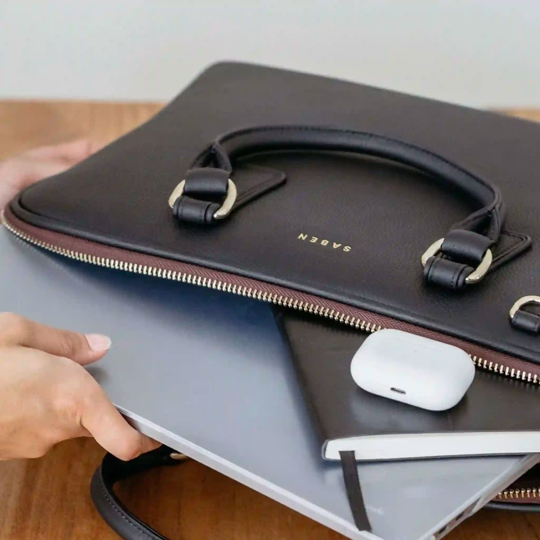 Black leather sleeve with gold zipper holding a laptop and white mouse on a wooden surface.
