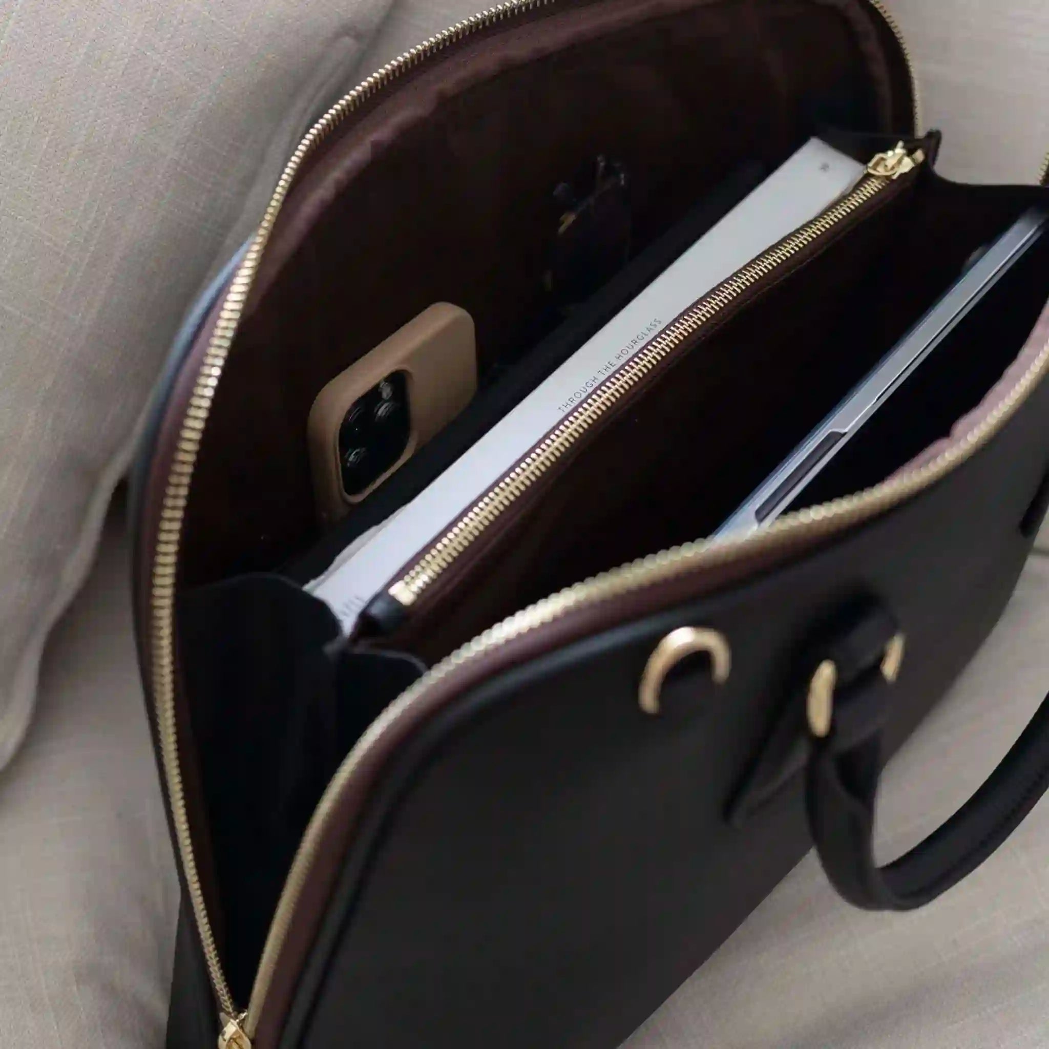 Open black leather briefcase with a phone and pen inside on a light gray surface