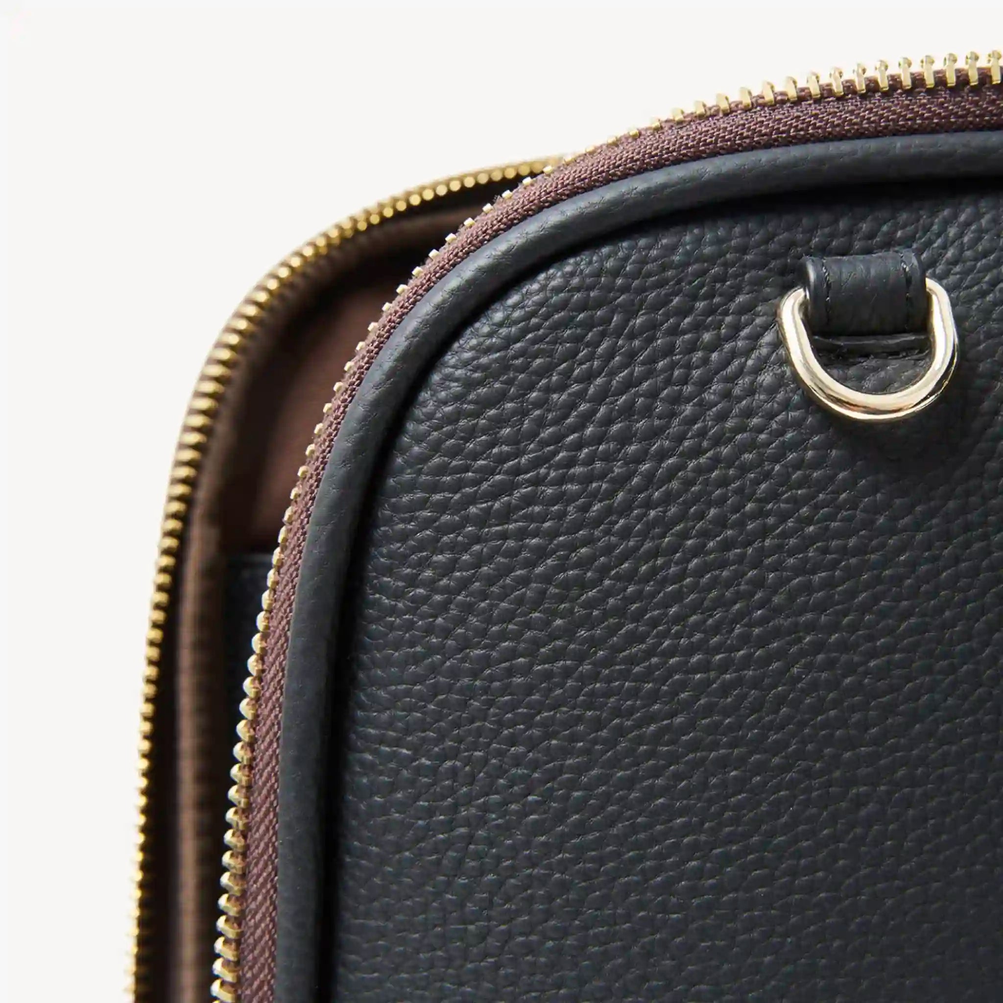 Close-up of a black leather bag with gold zipper and clasp on a white background