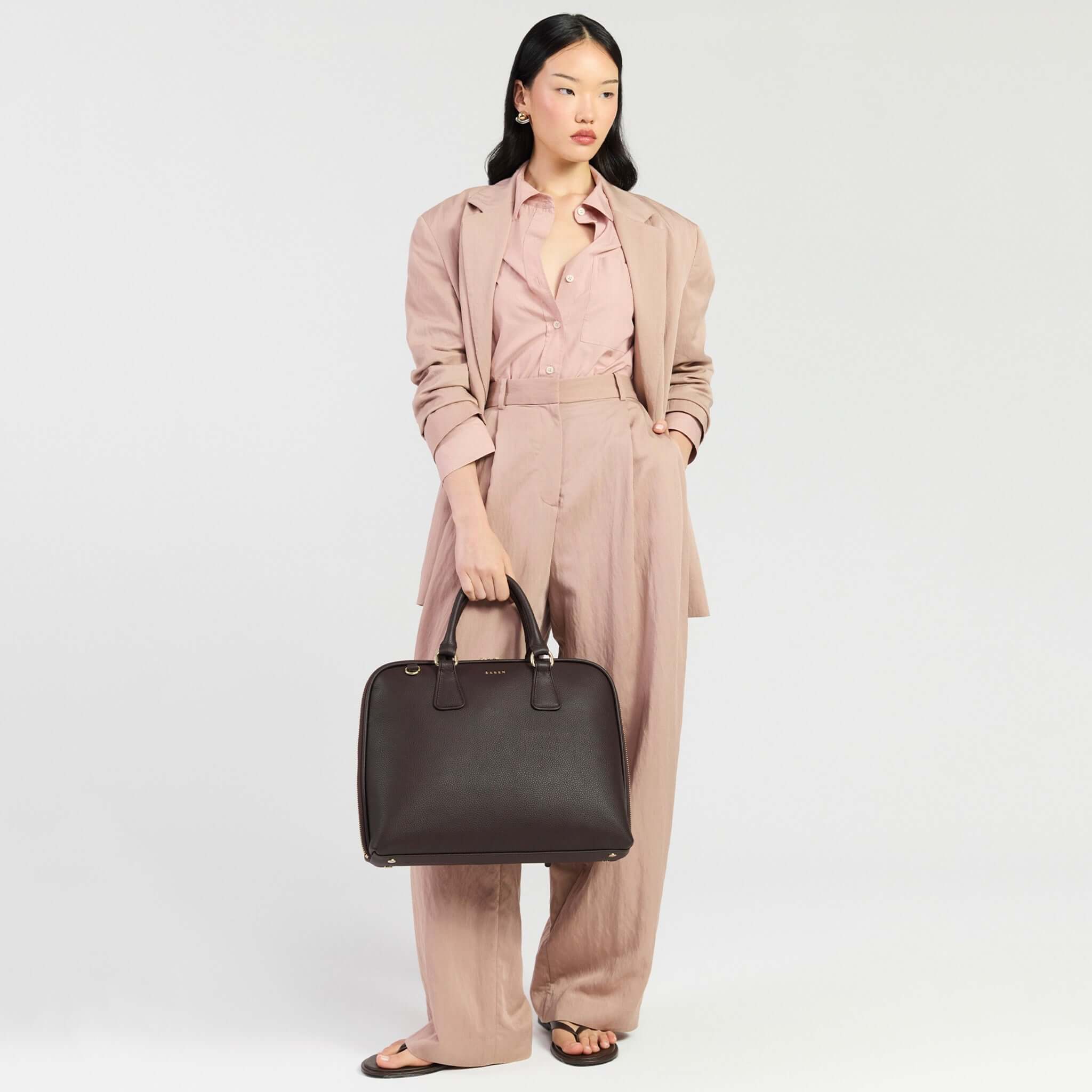 Saben Parker Briefcase - Cacao held by a woman in a stylish pink suit, embodying modern professional fashion.