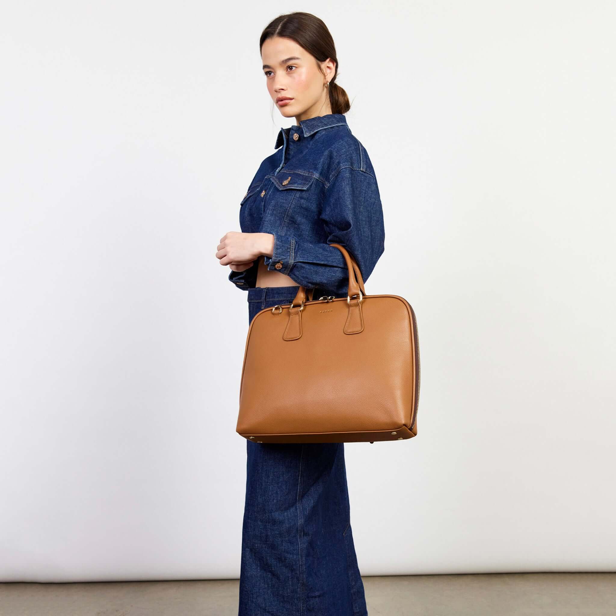 Alt Tag: Saben Parker Briefcase - Toffee carried by model in denim outfit, sleek tan leather laptop briefcase for work and travel