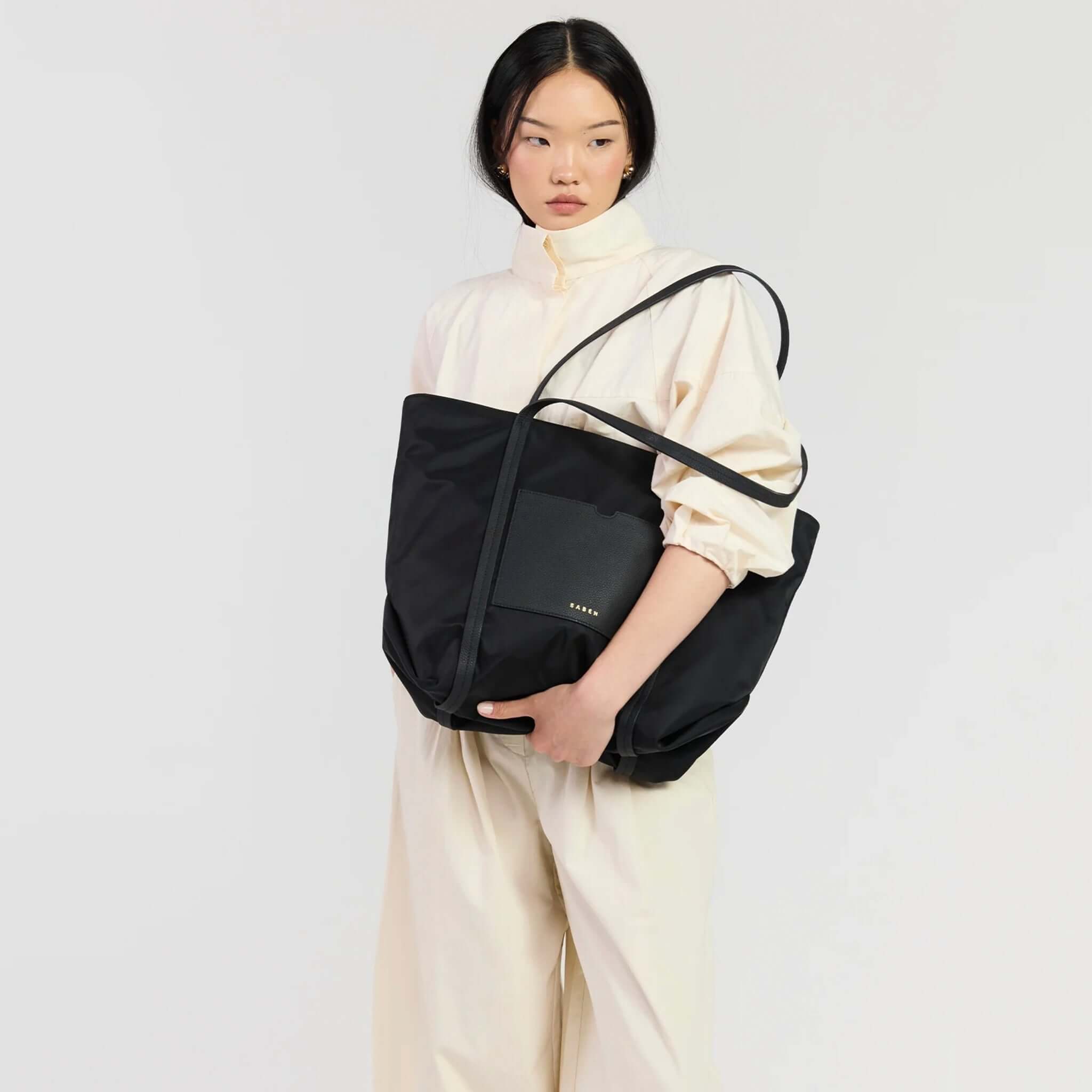 Saben Porter Tote - Black Recycled Nylon being held by a woman in a light blouse, showcasing its stylish design.