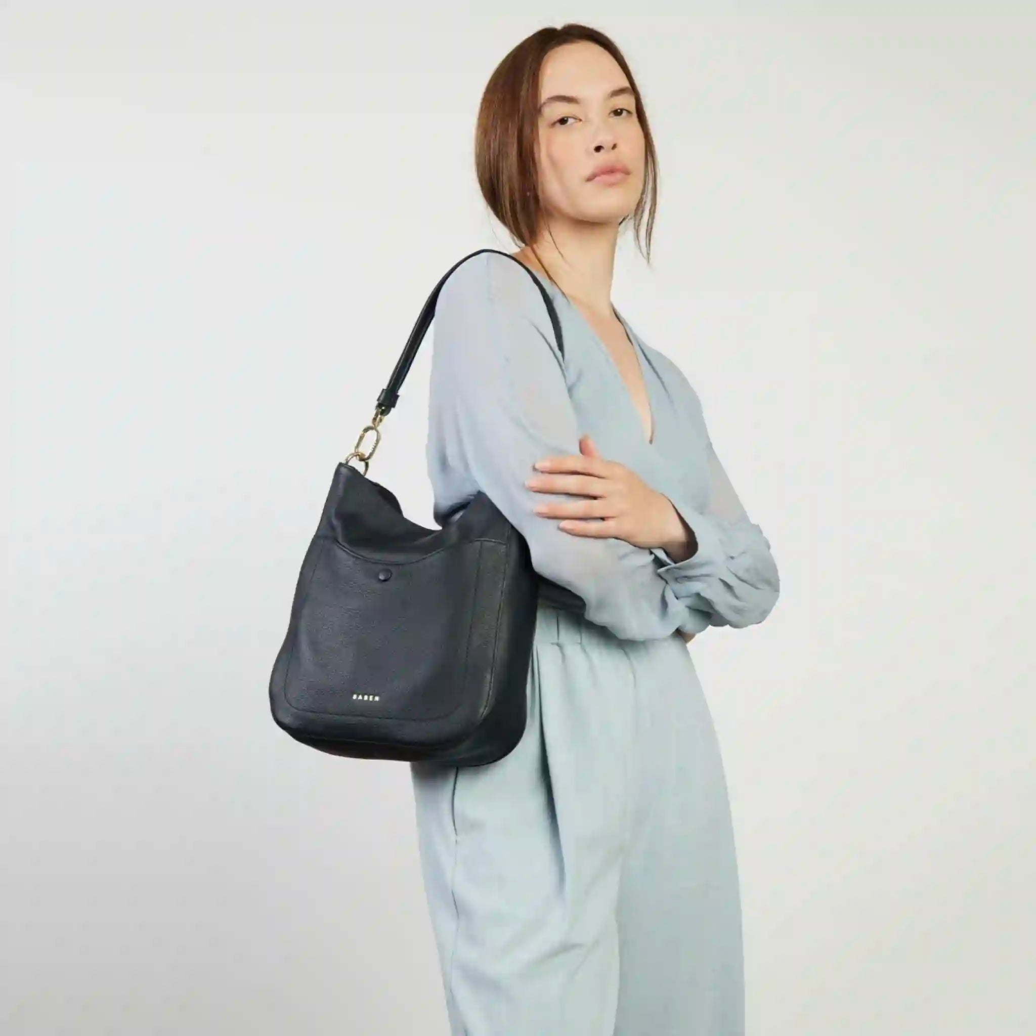 Woman holding a black handbag against a plain background