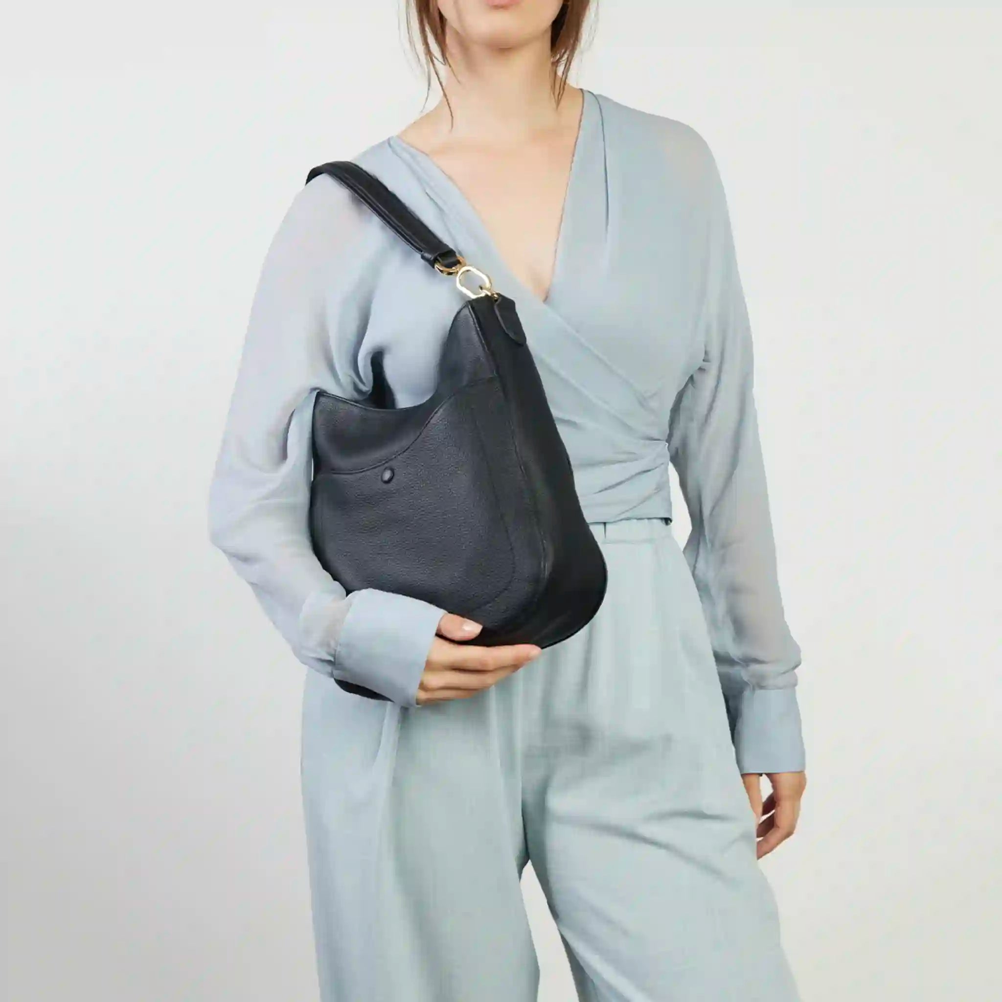 Person wearing a light gray outfit holding a black handbag against a plain background