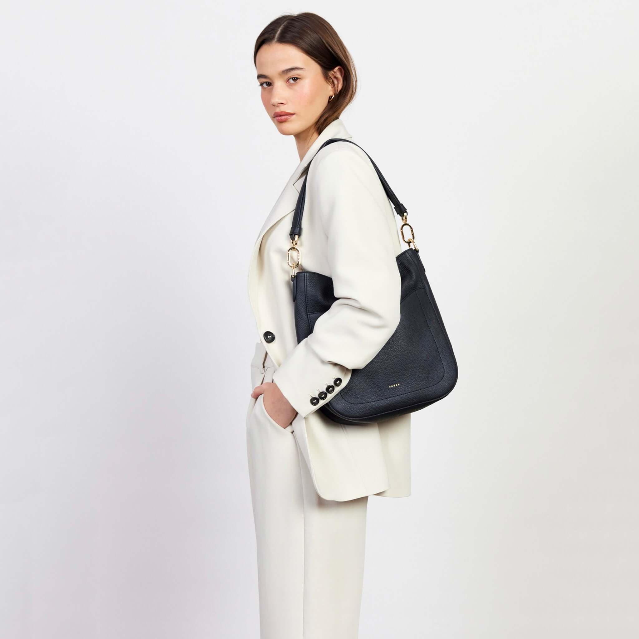 Alt Tag: Saben Rebe Shoulder Bag - Black Luxe black pebbled leather hobo bag on shoulder with gold hardware, front pocket