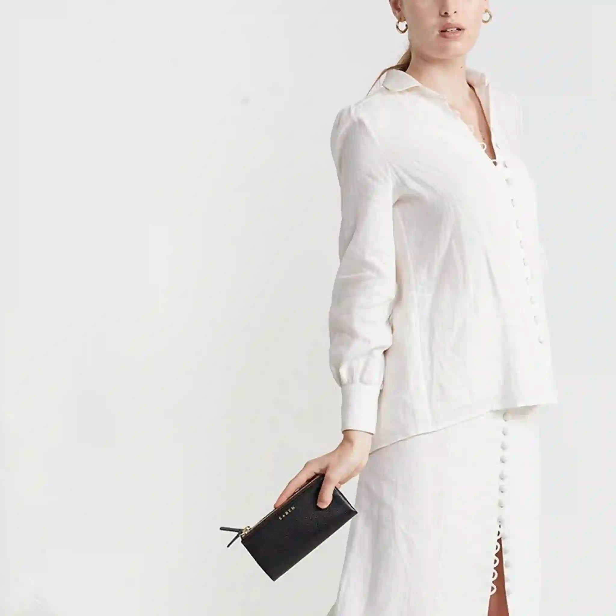 Person wearing a white outfit with a black wallet against a white background