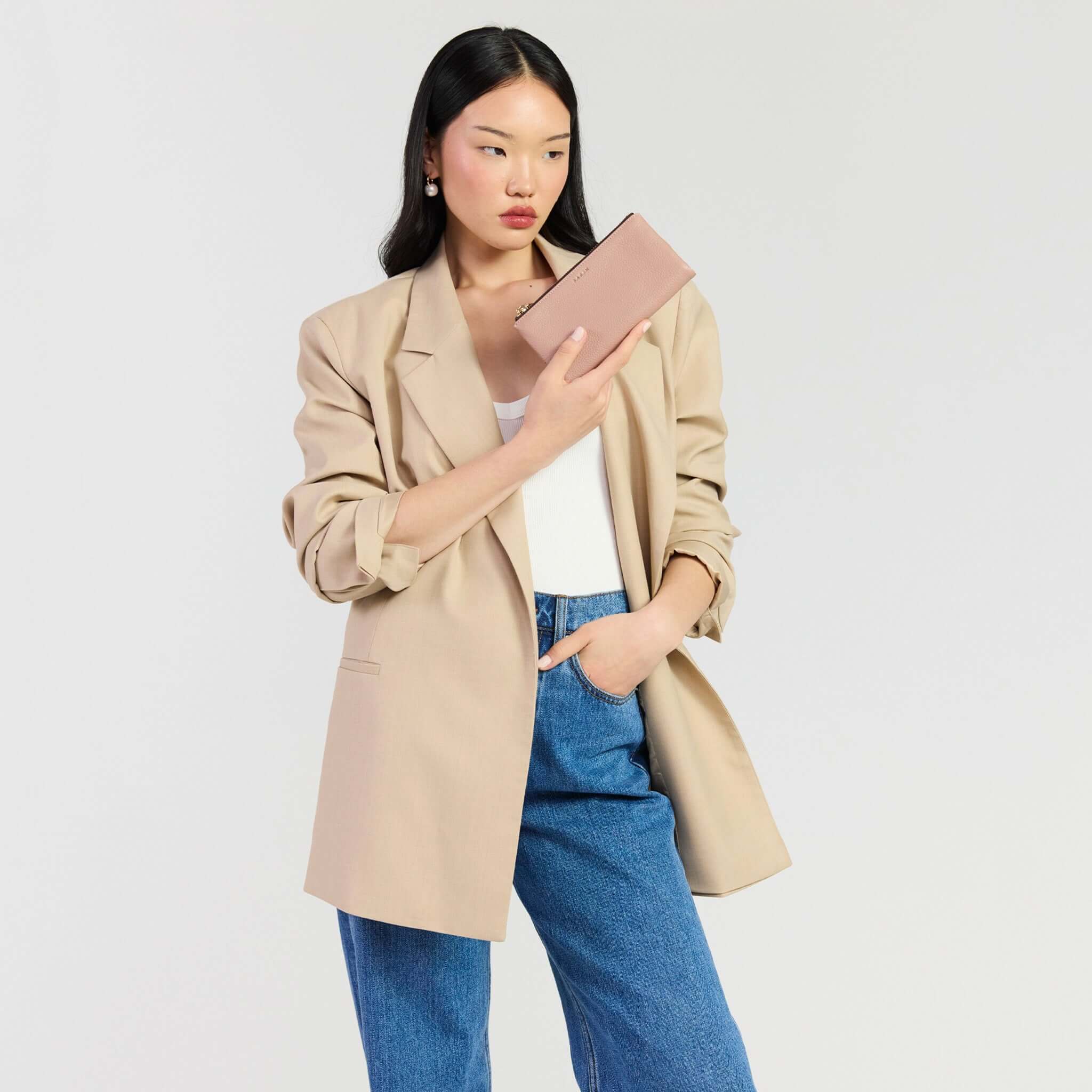 Model holding the Saben Sam Wallet - Rosewater, wearing a stylish blazer and denim jeans.