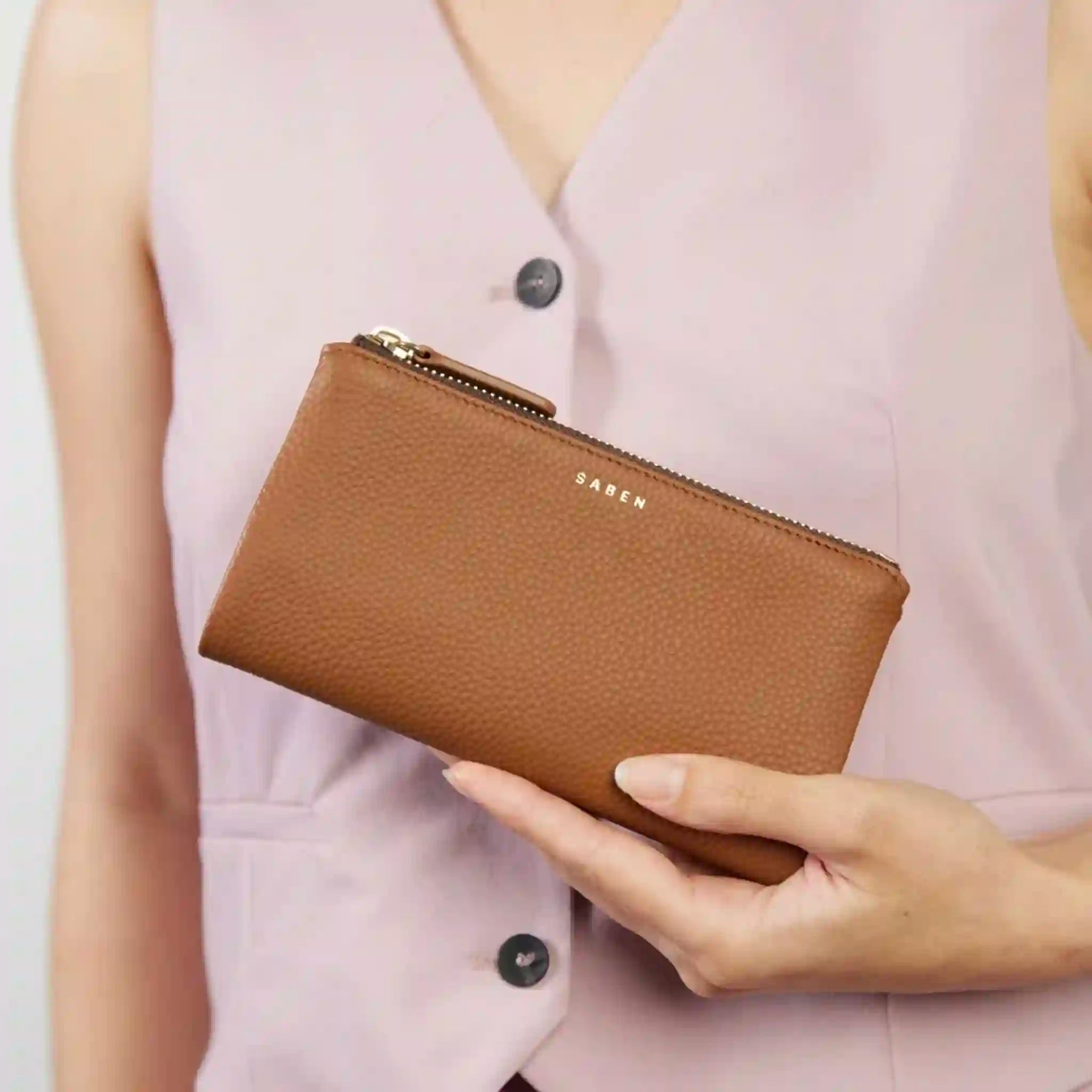 Brown wallet held by a person wearing a light pink sleeveless top.