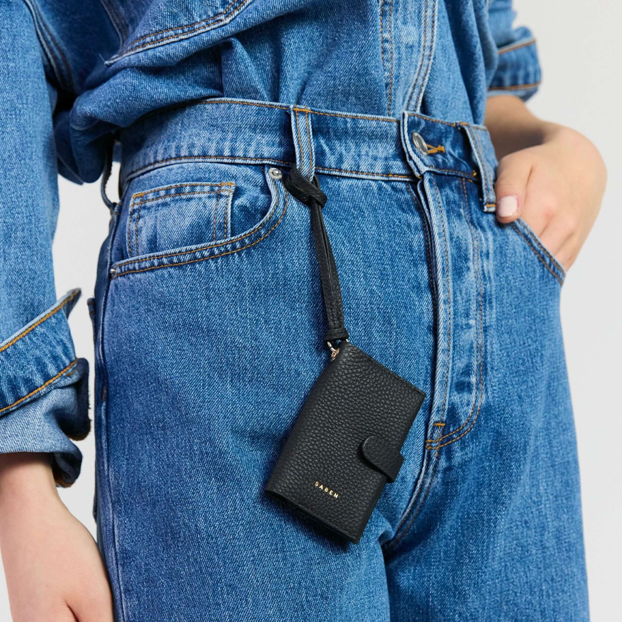 Saben Sid Card Holder - Black attached to a pair of denim jeans with a wristlet strap.