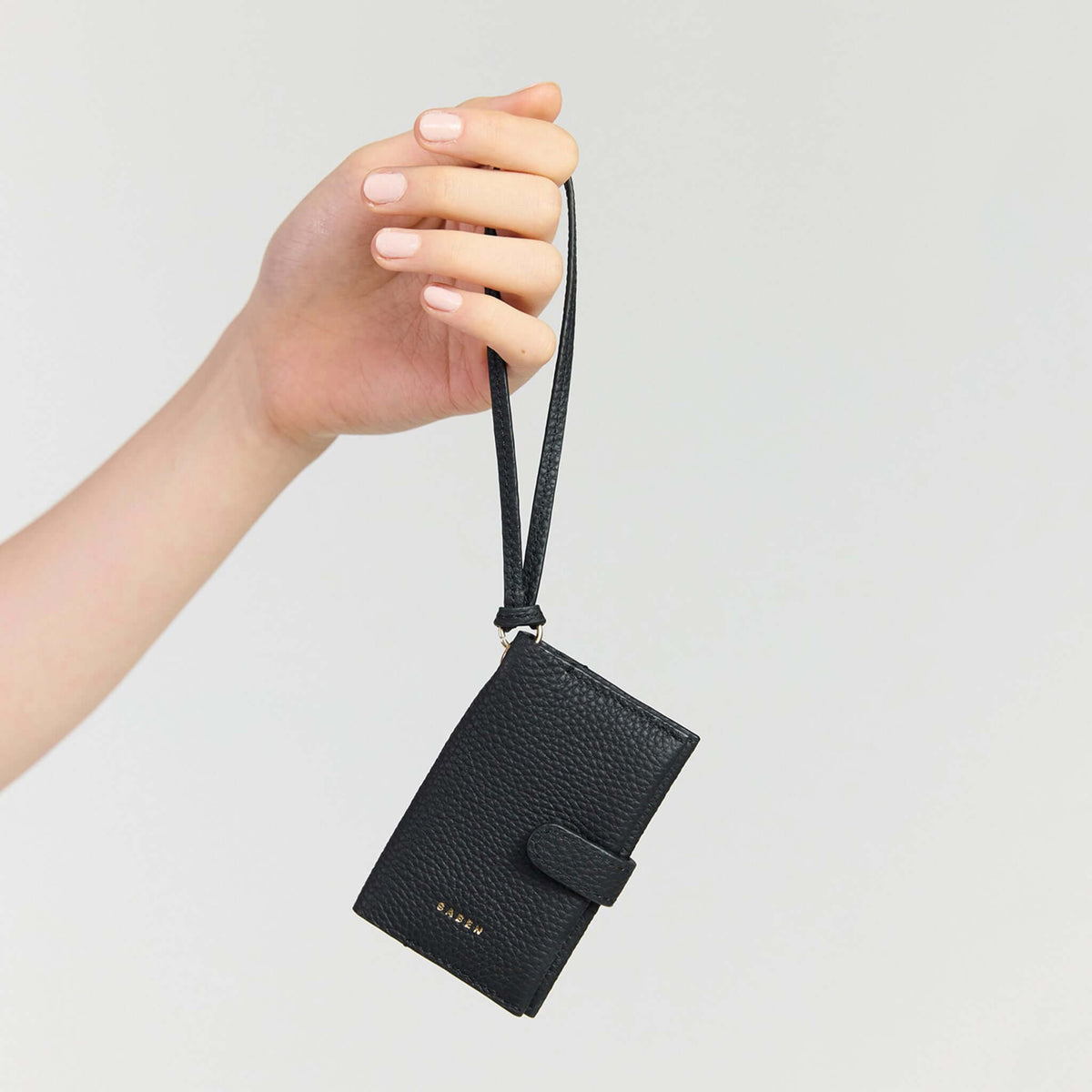 Saben Sid Card Holder - Black held by a hand with a wristlet strap, showcasing its compact design.