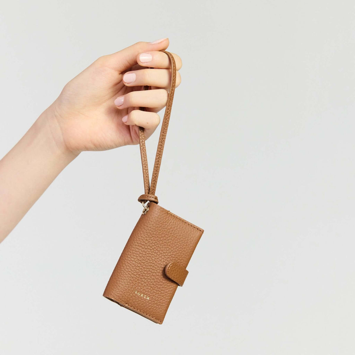 Saben Sid Card Holder - Tan held by hand with wristlet strap for easy carrying and organization.