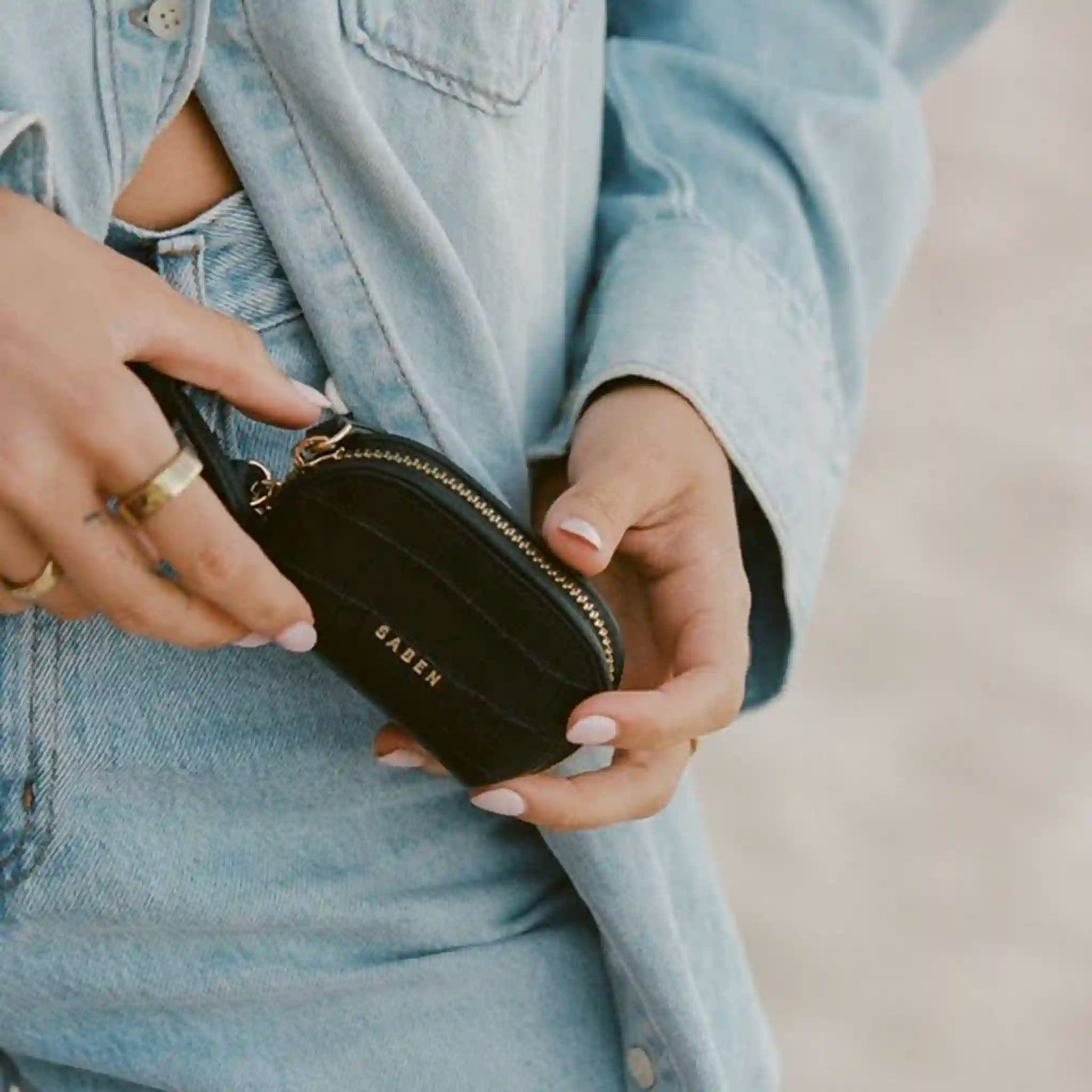 Person holding a black wallet with 'Saben' branding, wearing a denim jacket.
