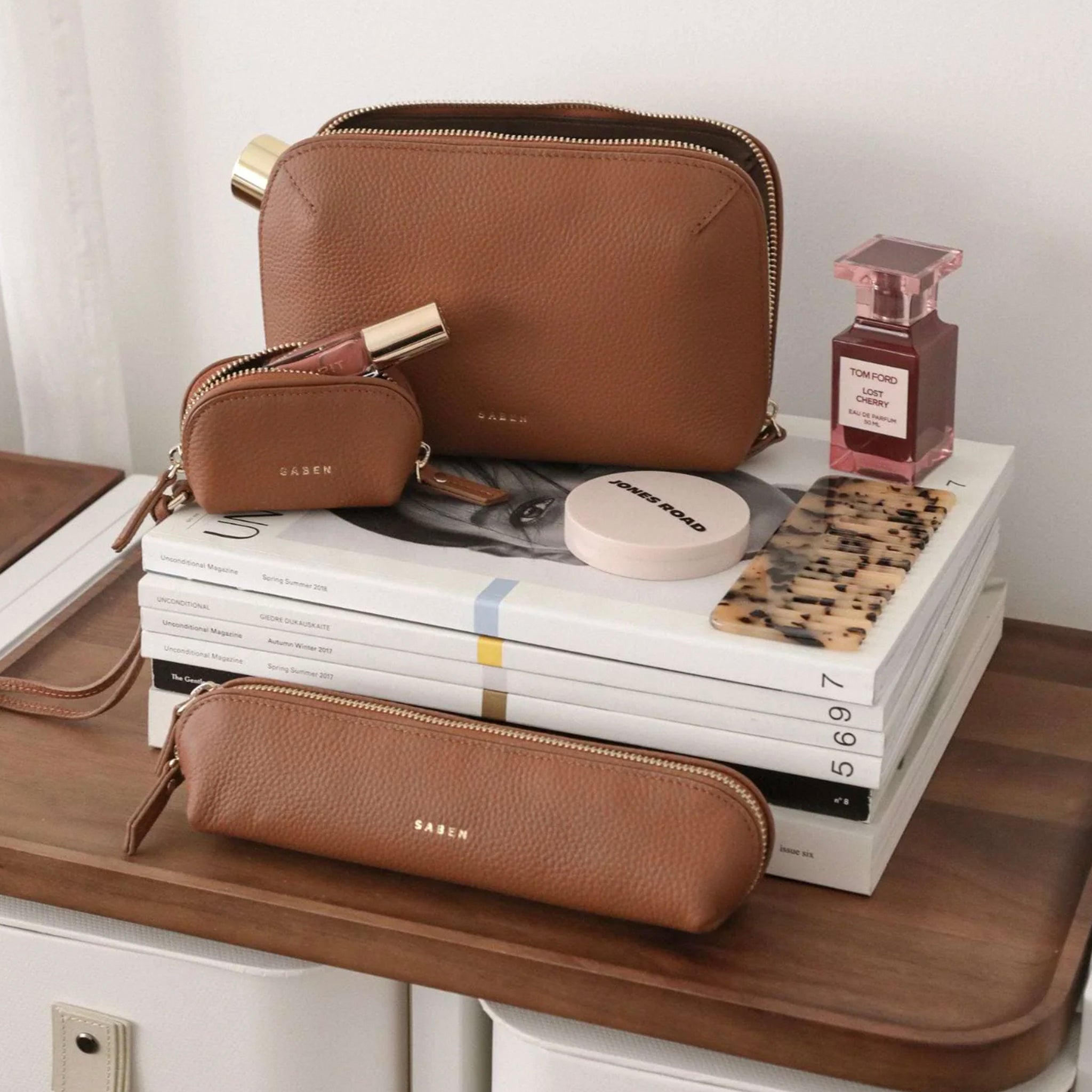 Brown leather pouches on a stack of books with a small bottle of perfume.