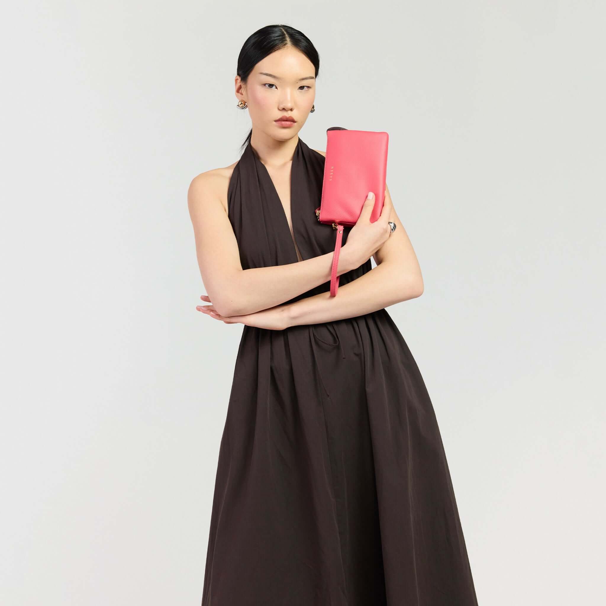 Saben Tilly Crossbody Bag - Azalea styled as a clutch, held by a model in a black dress.