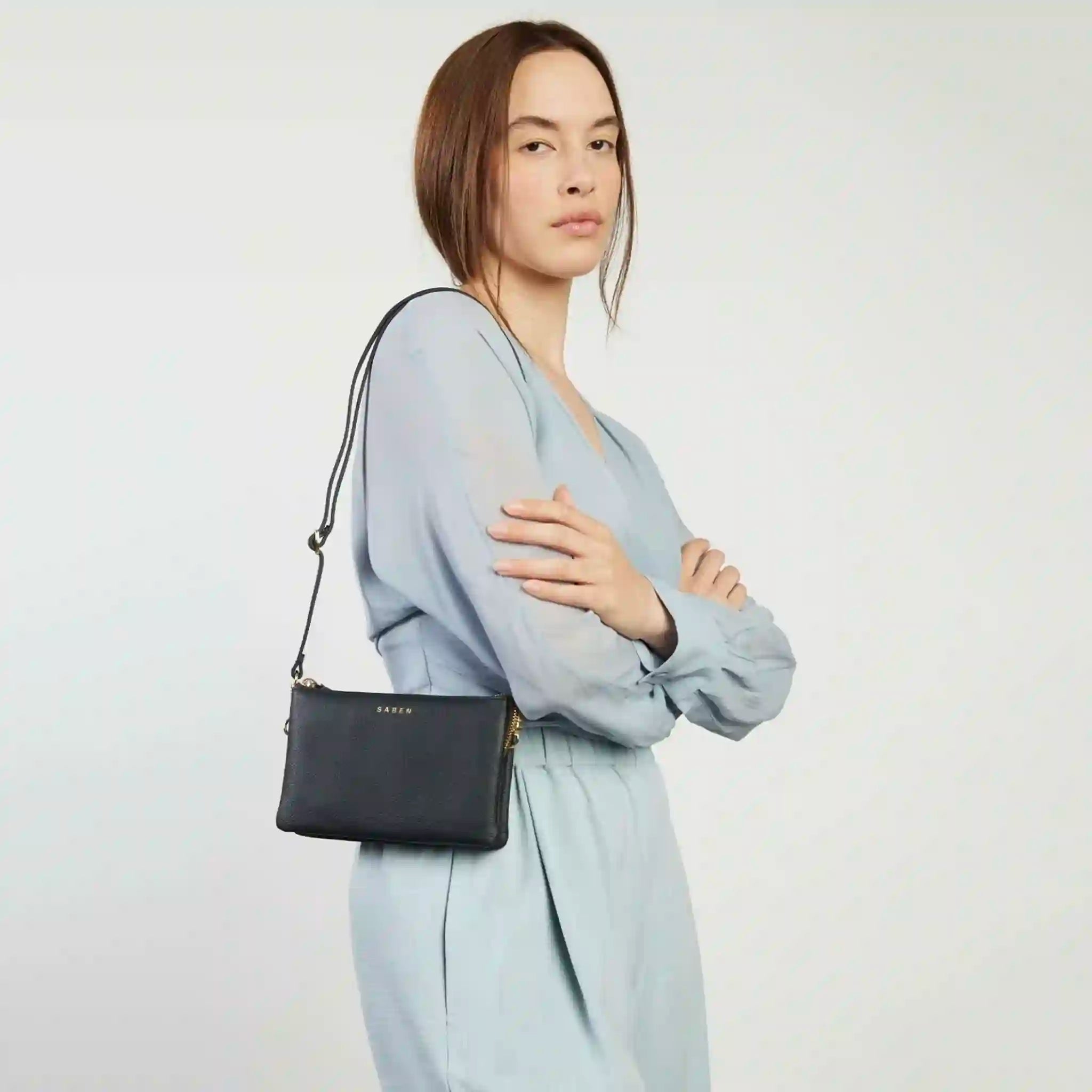 Woman holding a black handbag with a visible brand logo on a white background