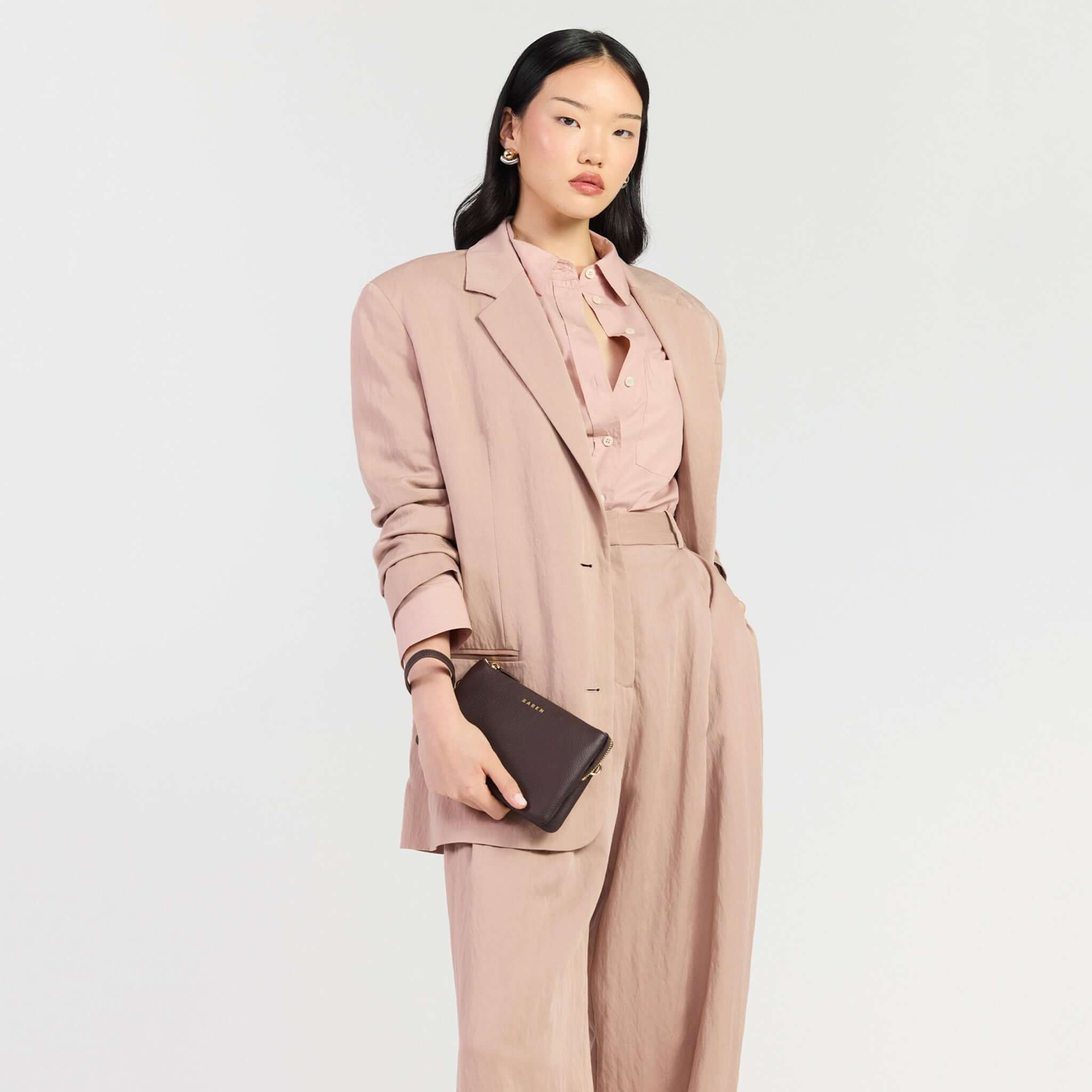 Saben Tilly Crossbody Bag - Cacao held by a model in a stylish pink outfit, showcasing versatility and elegance.
