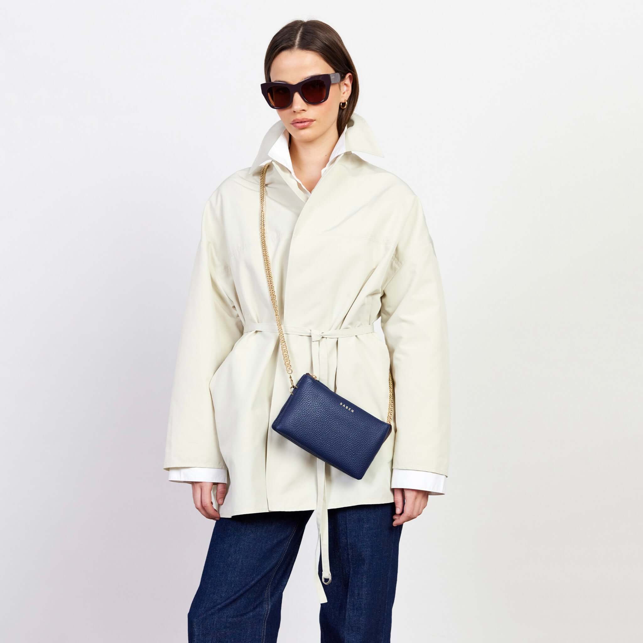 Saben Tilly Crossbody Bag - Ink styled with a chic outfit featuring a cream coat and sunglasses.