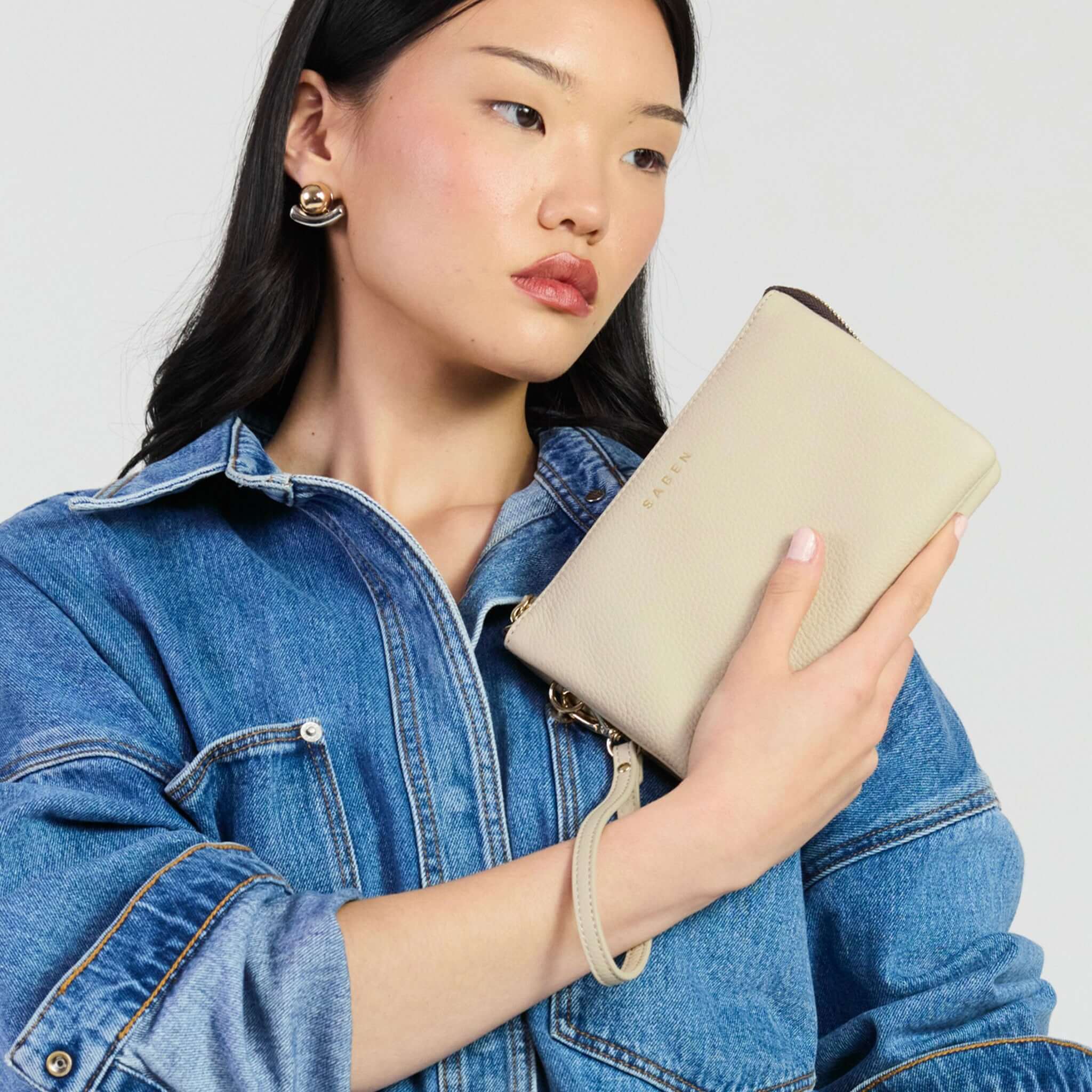 Saben Tilly Crossbody Bag - Oyster being held by a model in a denim jacket.