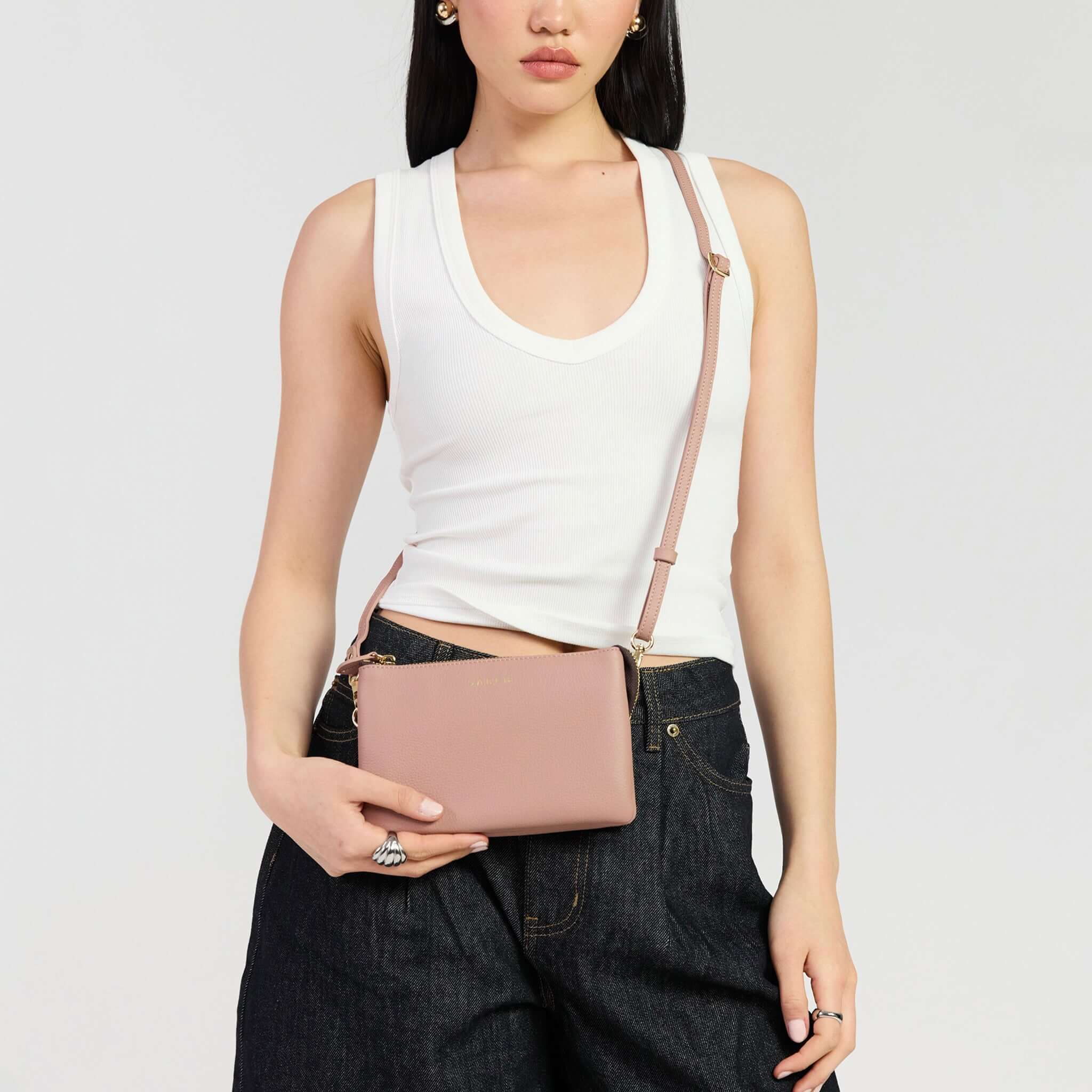Saben Tilly Crossbody Bag - Rosewater being worn as a clutch by a model in casual attire.