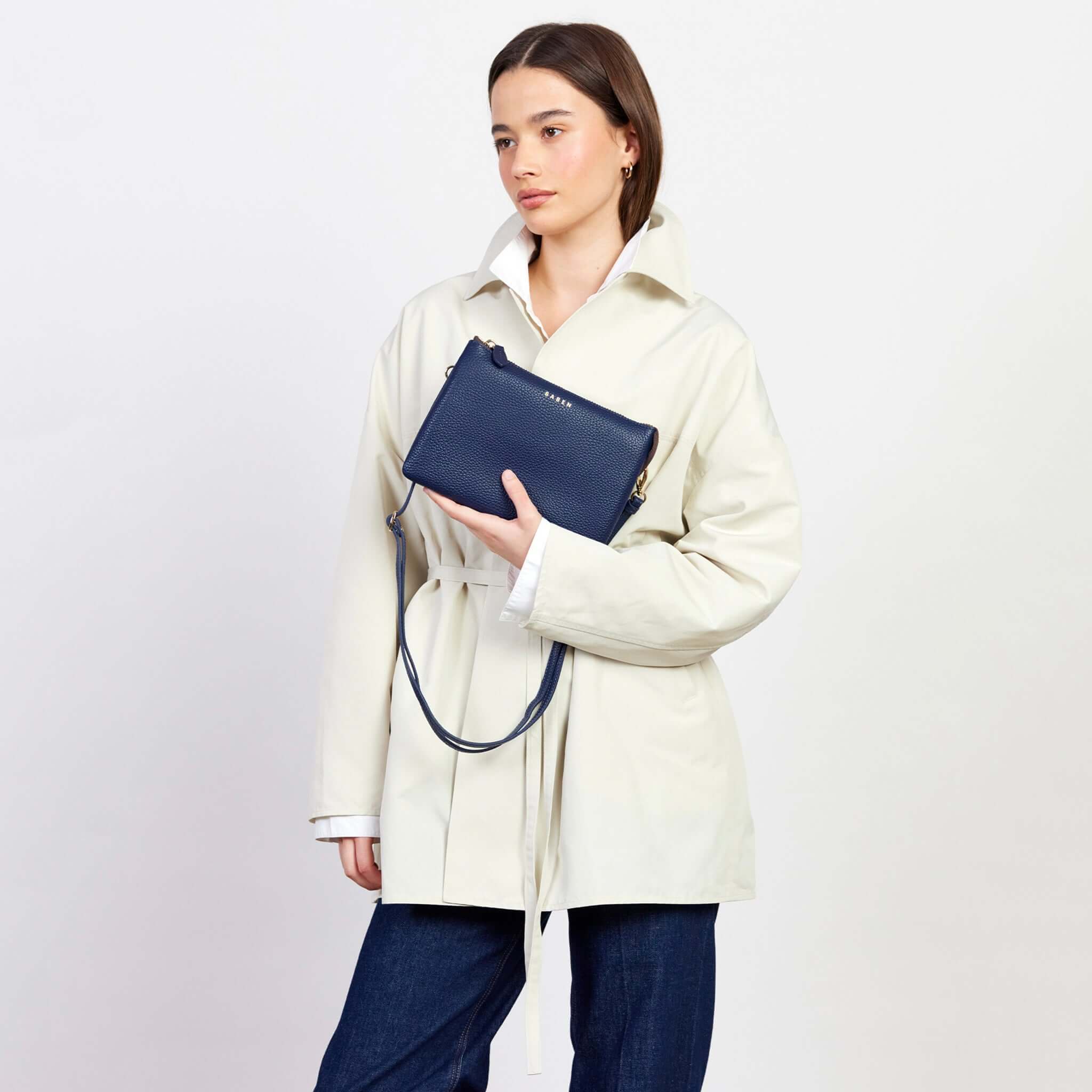 Woman in a cream coat holding Saben Tilly's Big Sis Crossbody Bag - Ink, showcasing its stylish versatility.