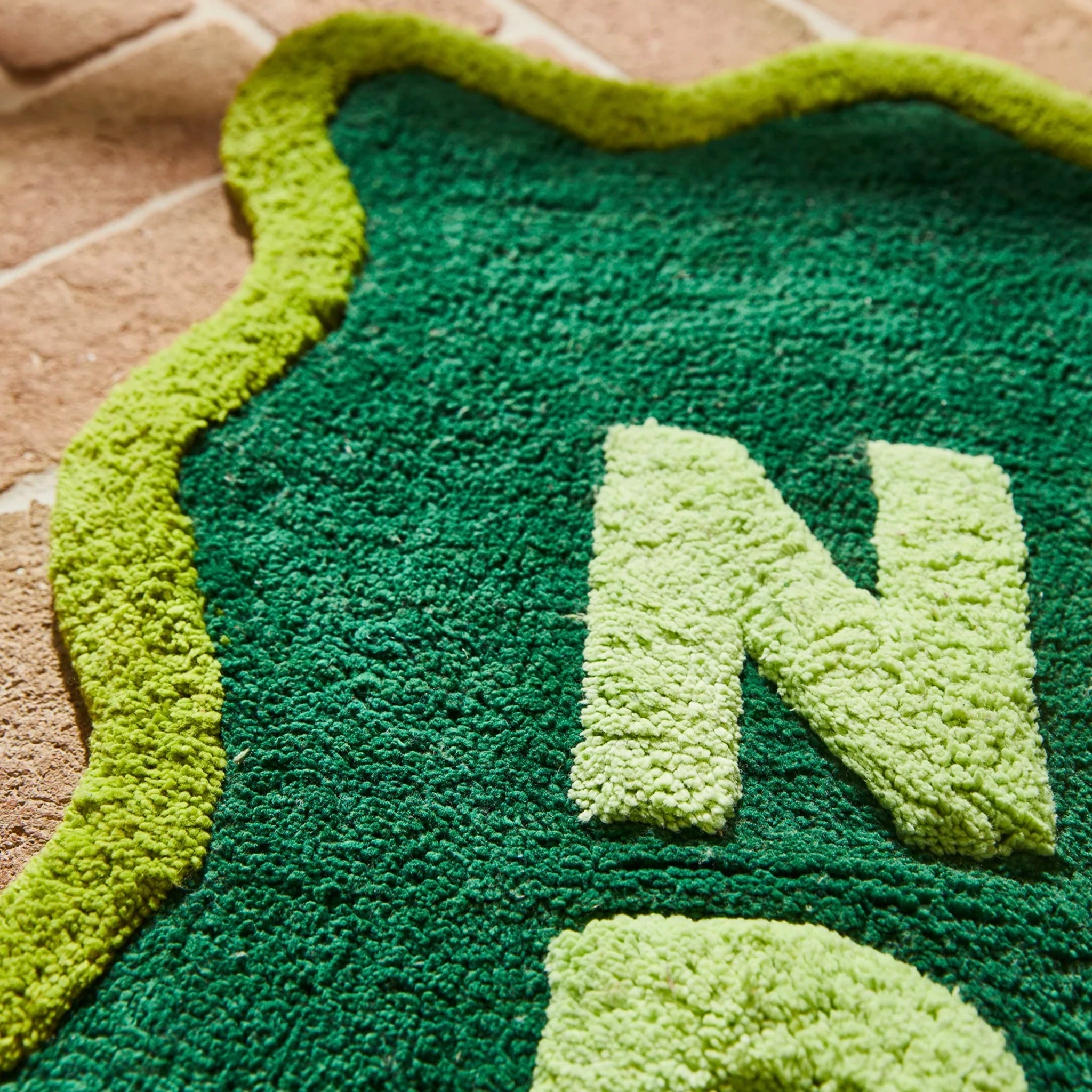Green textured bath mat with a large letter 'N' on a brown surface