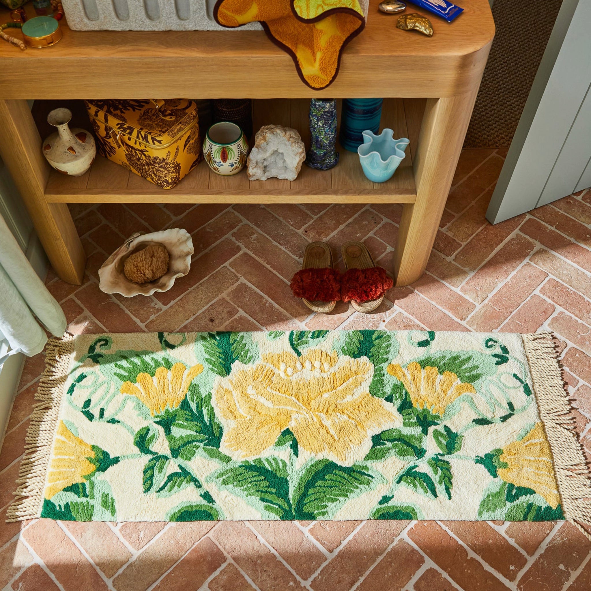 Floral bath mat on a brick floor with a wooden shelf in the background