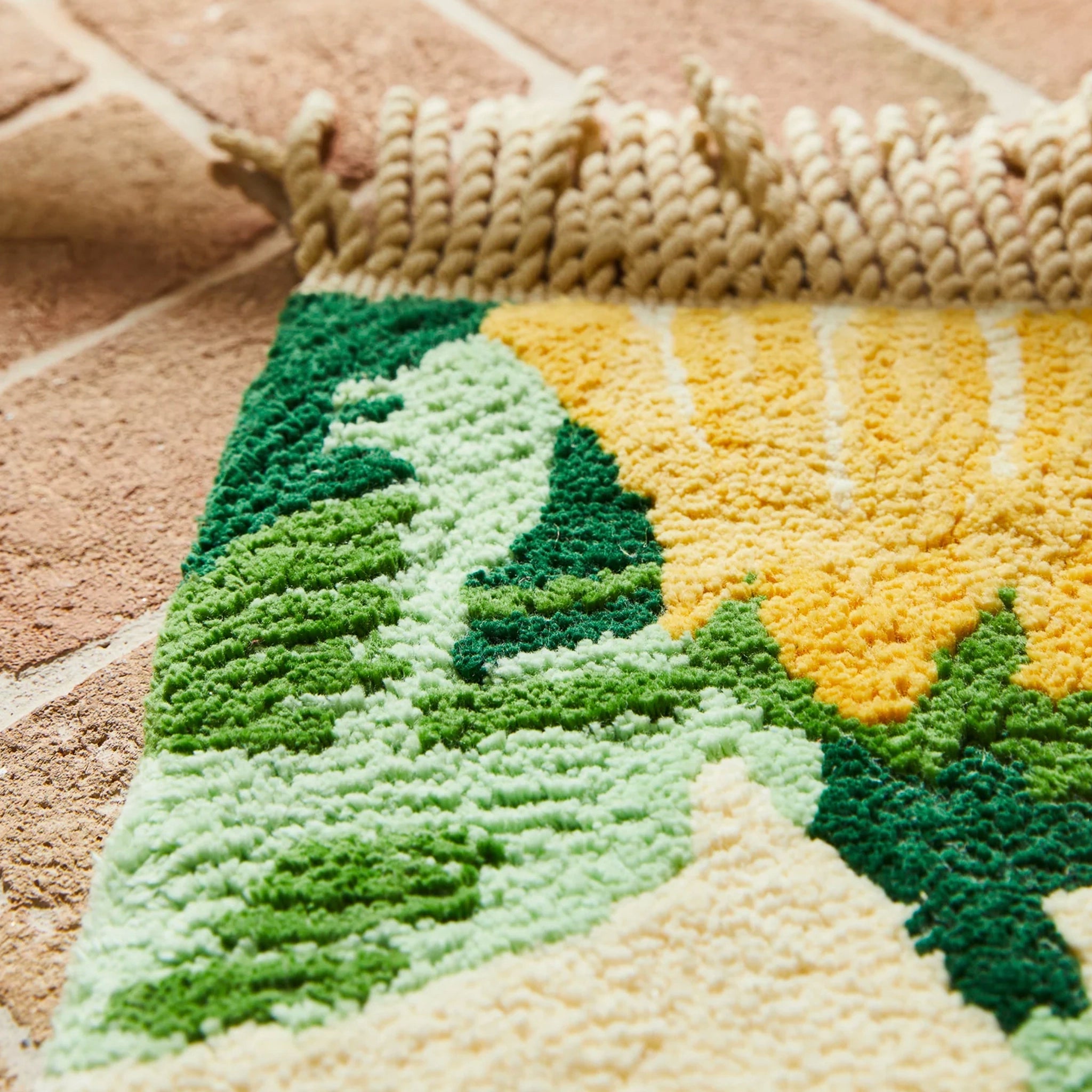 Close-up of a textured bath mat with green and yellow patterns on a stone floor.