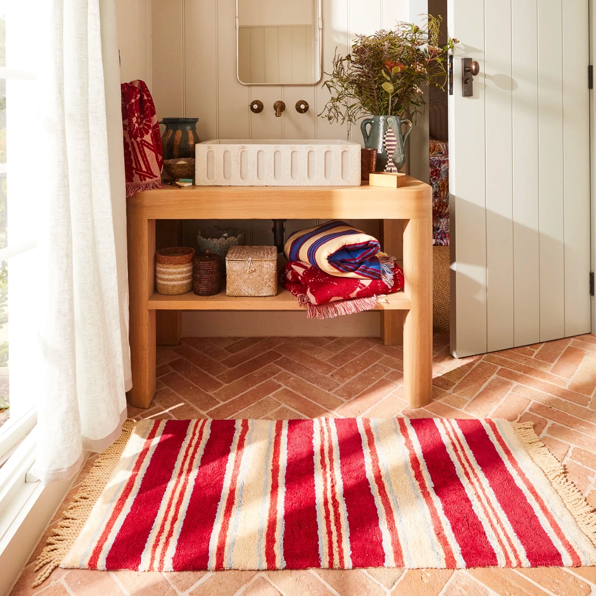 Bathroom with wooden vanity, sink, and striped bat mat on floor