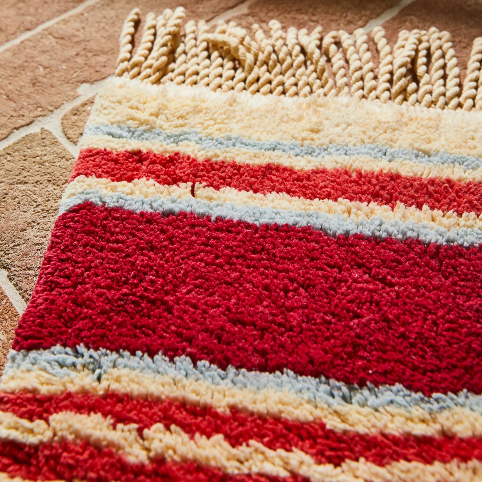 Striped bath mat with red, beige, and blue pattern on a textured surface