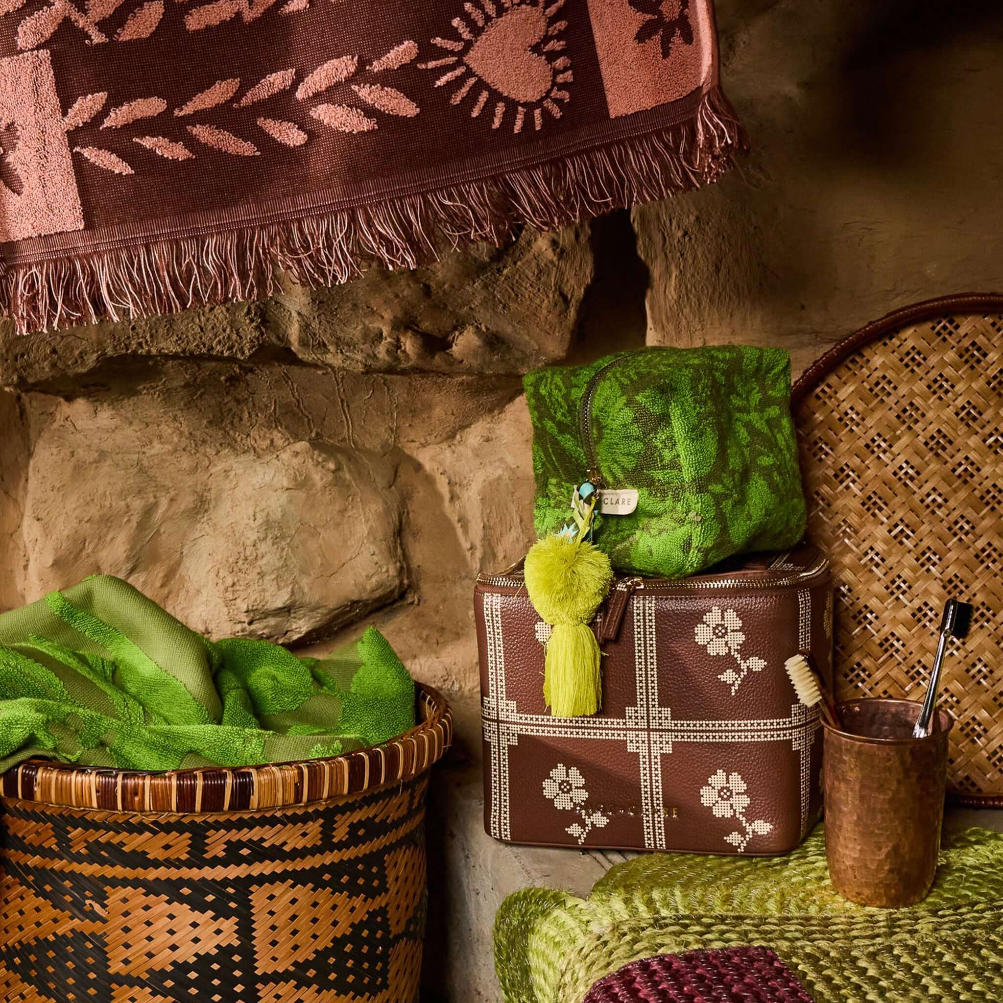 Sage x Clare Bonny Medium Vanity Case - Umber surrounded by vibrant green textiles and woven baskets.