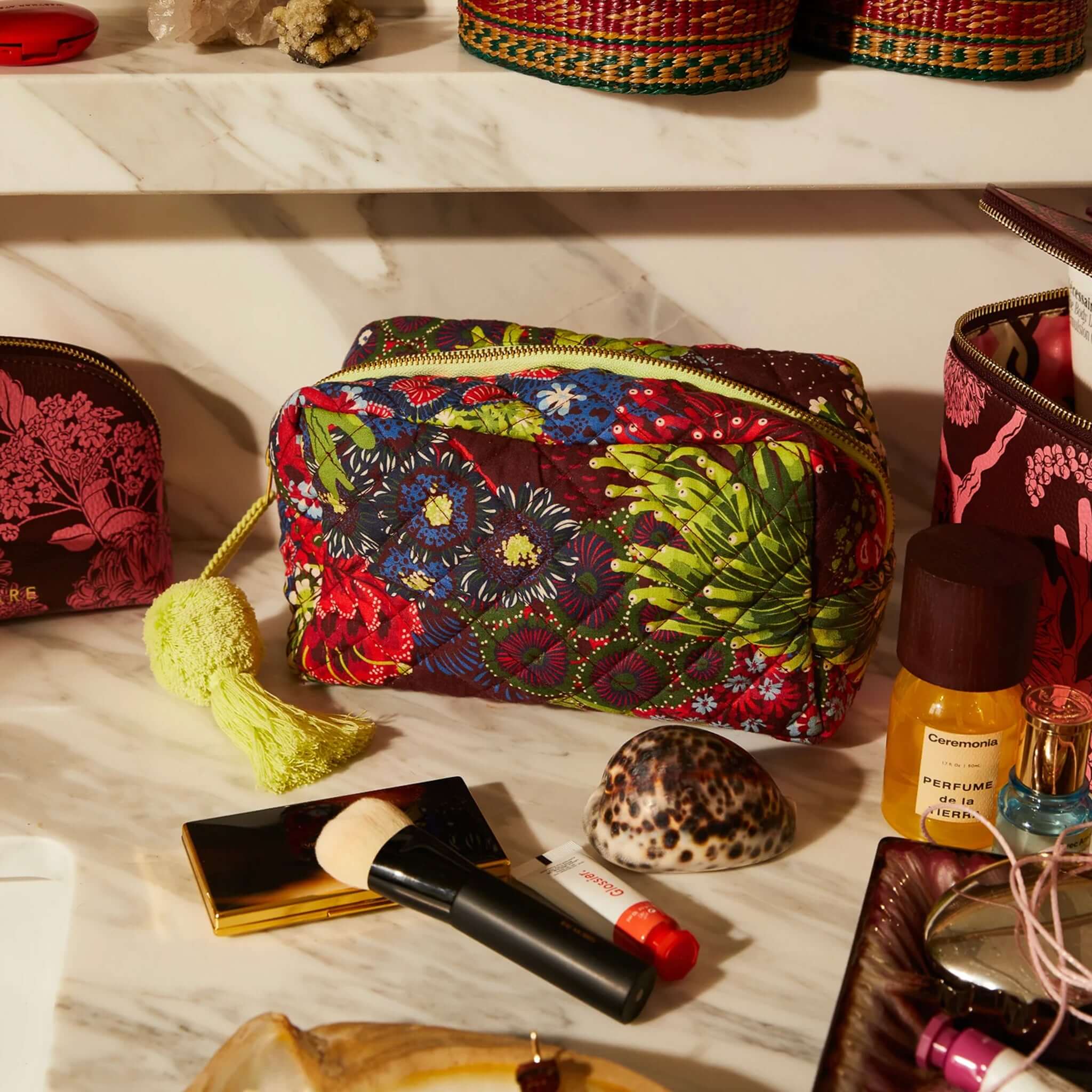 Sage x Clare Cora Organic Cotton Beauty Bag with vibrant floral print and lime green tassel on a marble surface.
