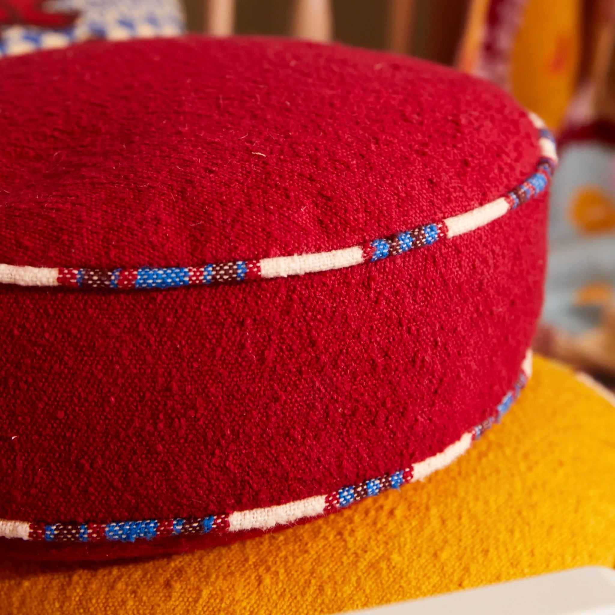 Red woven cushion with decorative band on a blurred background