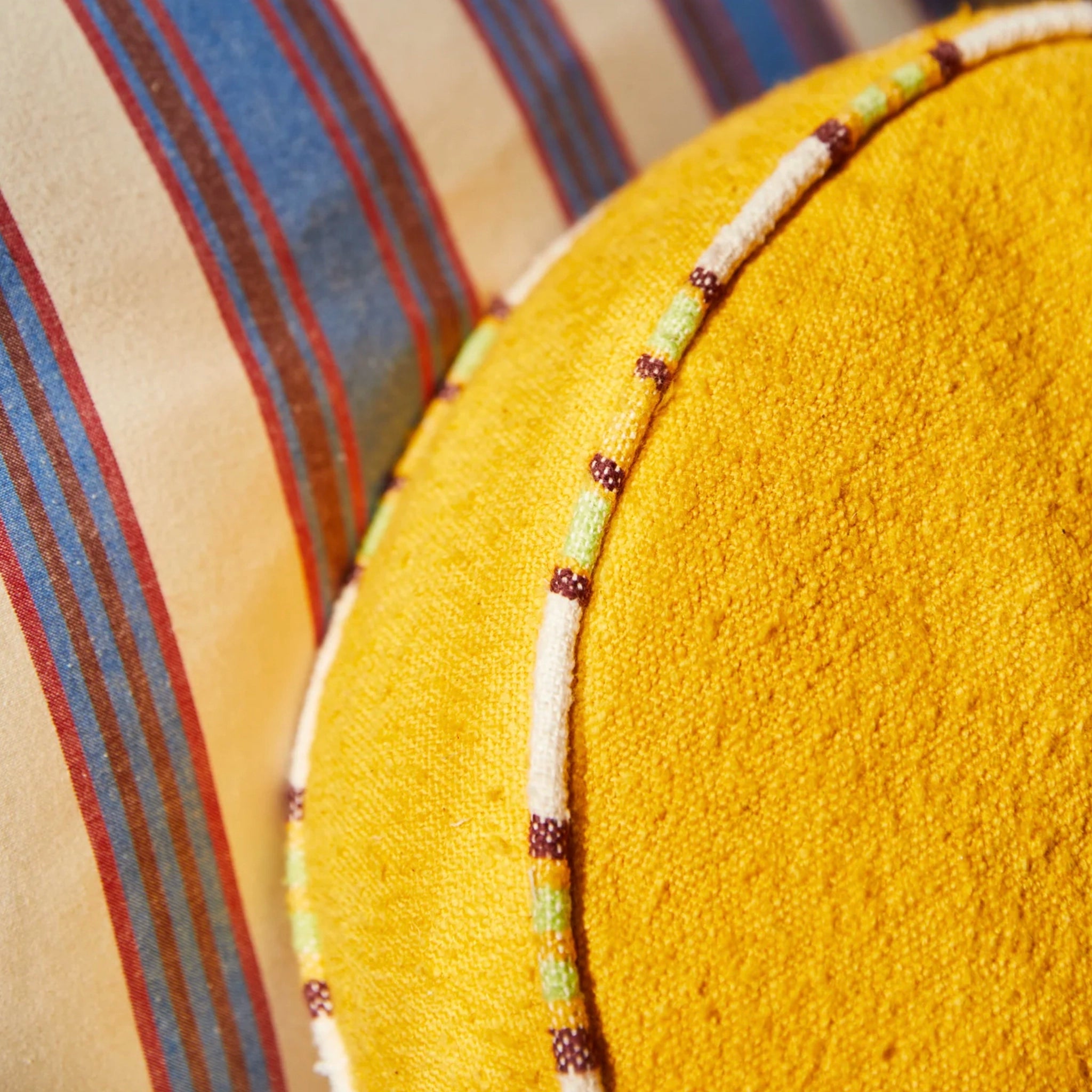 Close-up of a beaded cushion on a textured yellow surface with a striped fabric background.