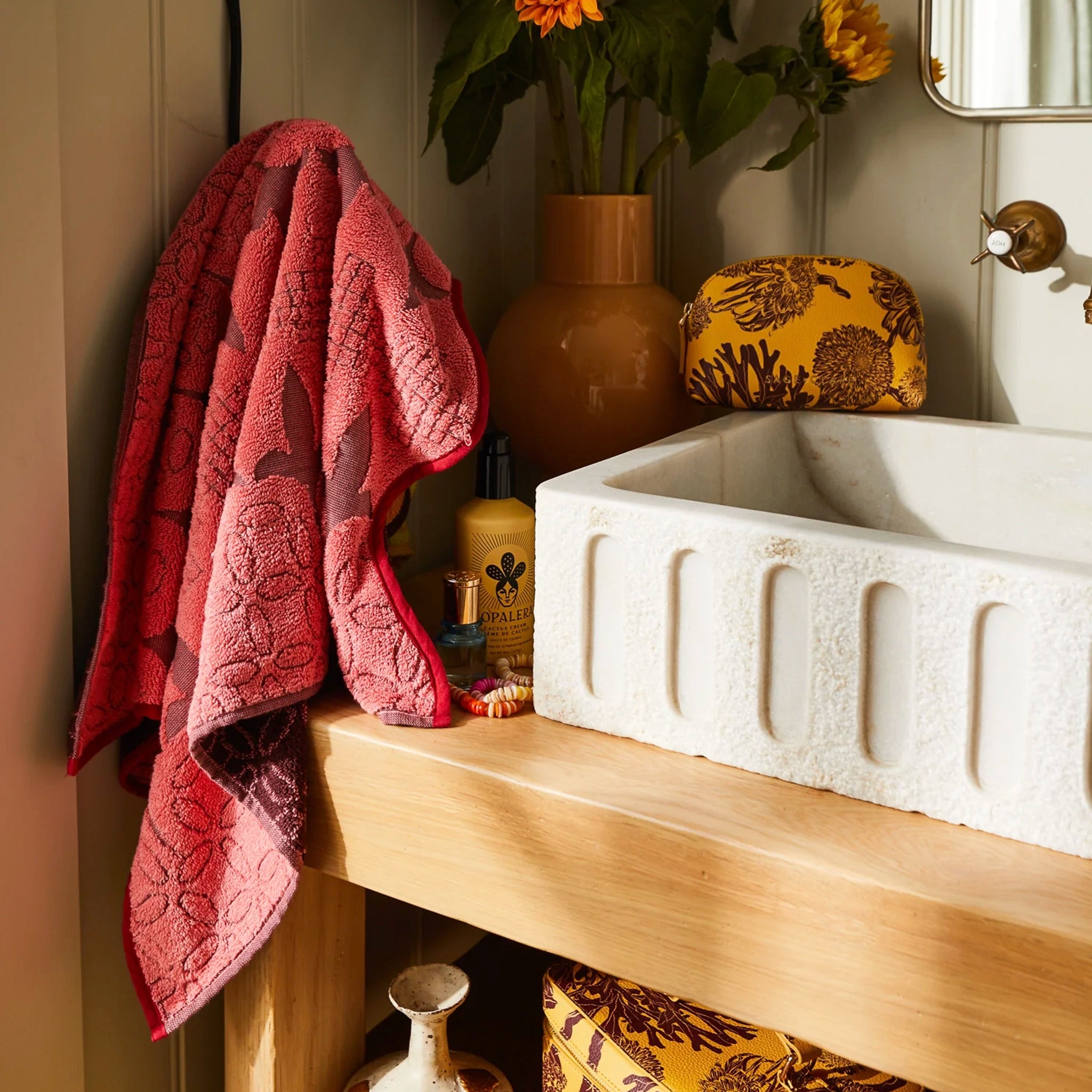 Red towel hanging over a wooden cabinet with a white sink and decorative items.